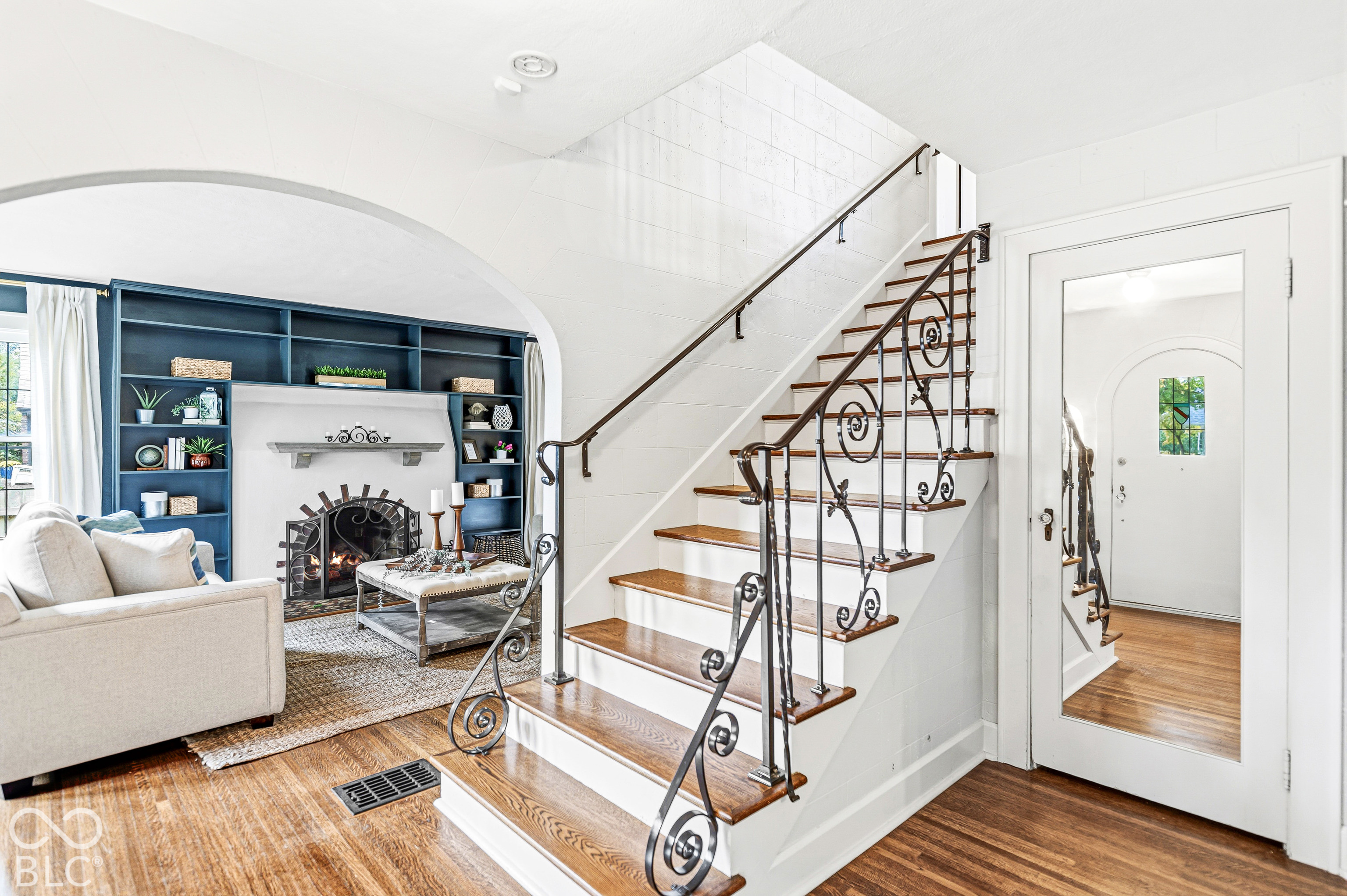 Staircase featuring wood treads and an ornate iron railing, archway detailing, fireplace with built-in shelving, and wood-finish flooring