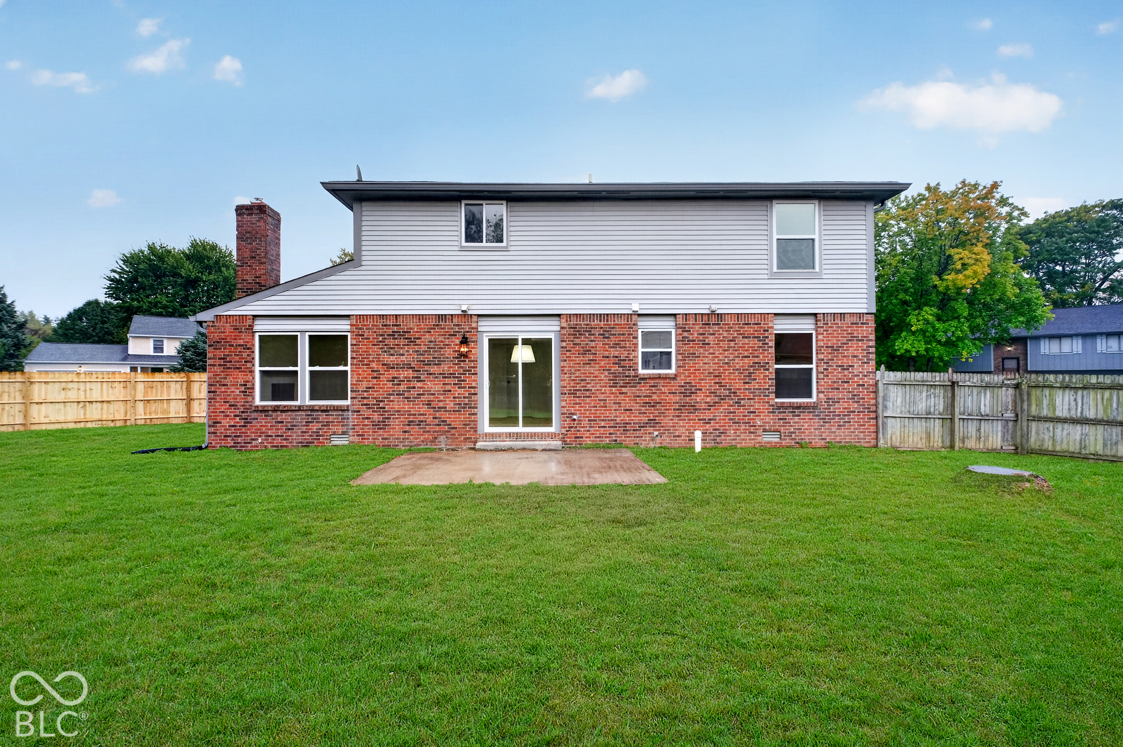 Rear exterior featuring a brick and vinyl siding facade, a concrete patio, a brick chimney, and a fenced-in grass backyard