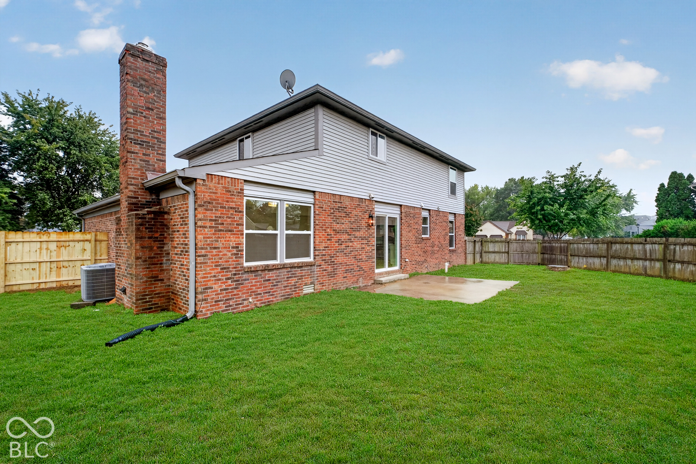 Rear exterior featuring a brick and vinyl siding facade, an exterior brick chimney, a concrete patio, and a fully fenced backyard