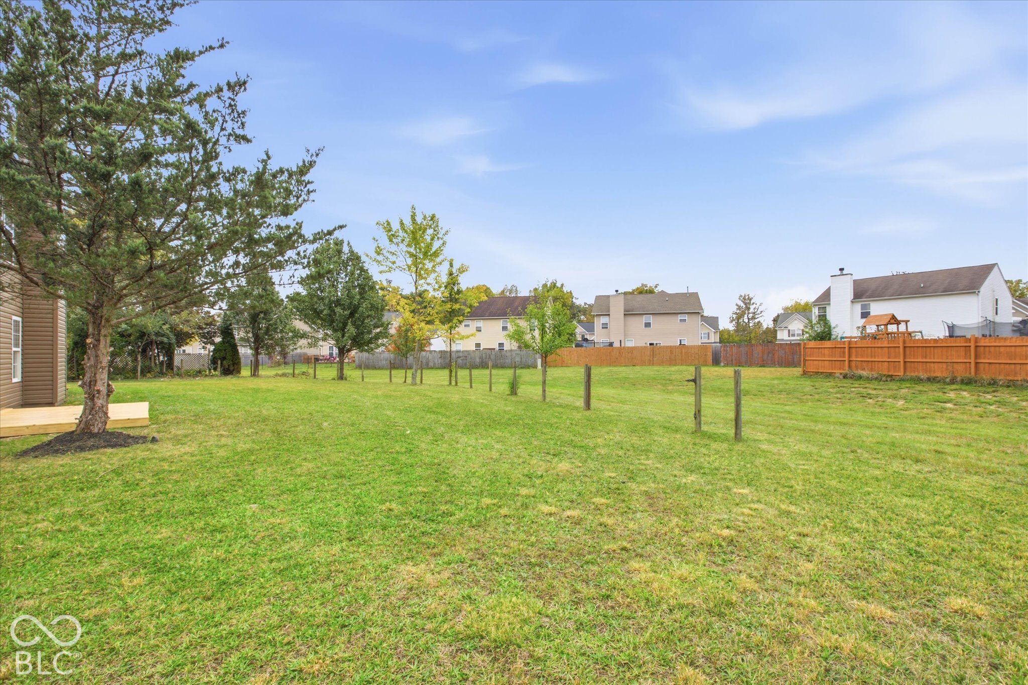 Expansive backyard featuring a manicured lawn, mature trees, wood-finish deck, and wood privacy fencing