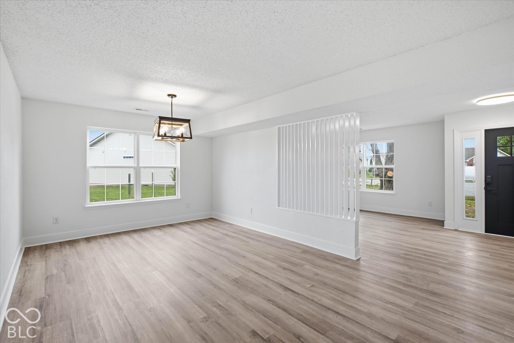 Interior space featuring wood-finish flooring, a decorative vertical slat room divider, a geometric pendant light fixture, and a dark-toned exterior entry door with glass pane detailing
