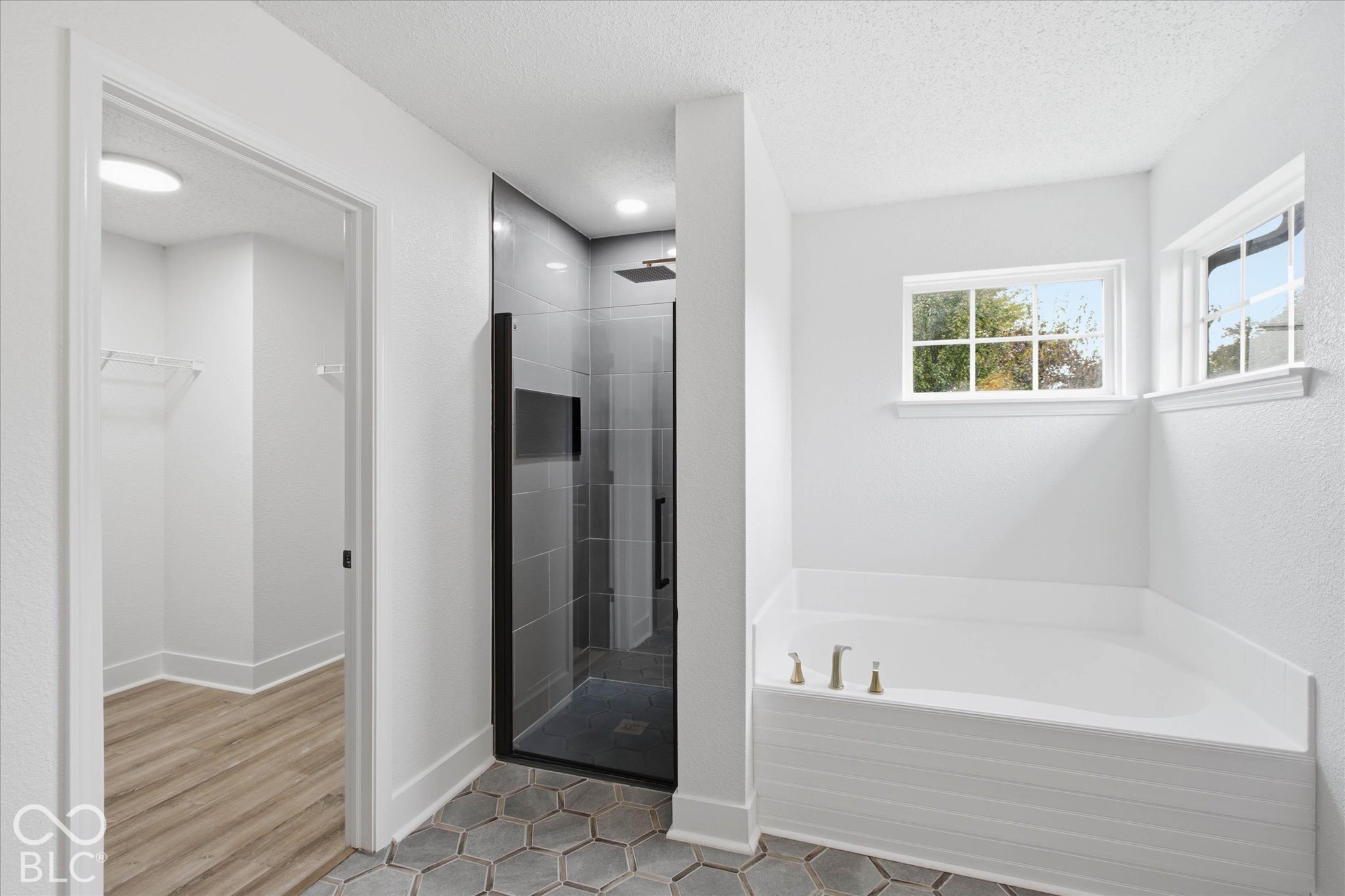 Bathroom featuring a walk-in shower with floor-to-ceiling tile, frameless glass enclosure, and rainfall showerhead, alongside a built-in soaking tub and hexagonal tile flooring