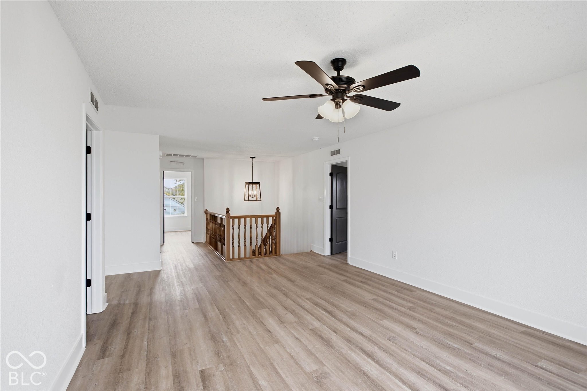 Wood-finish flooring, ceiling fan with integrated light fixture, and wooden staircase railing featuring decorative balusters