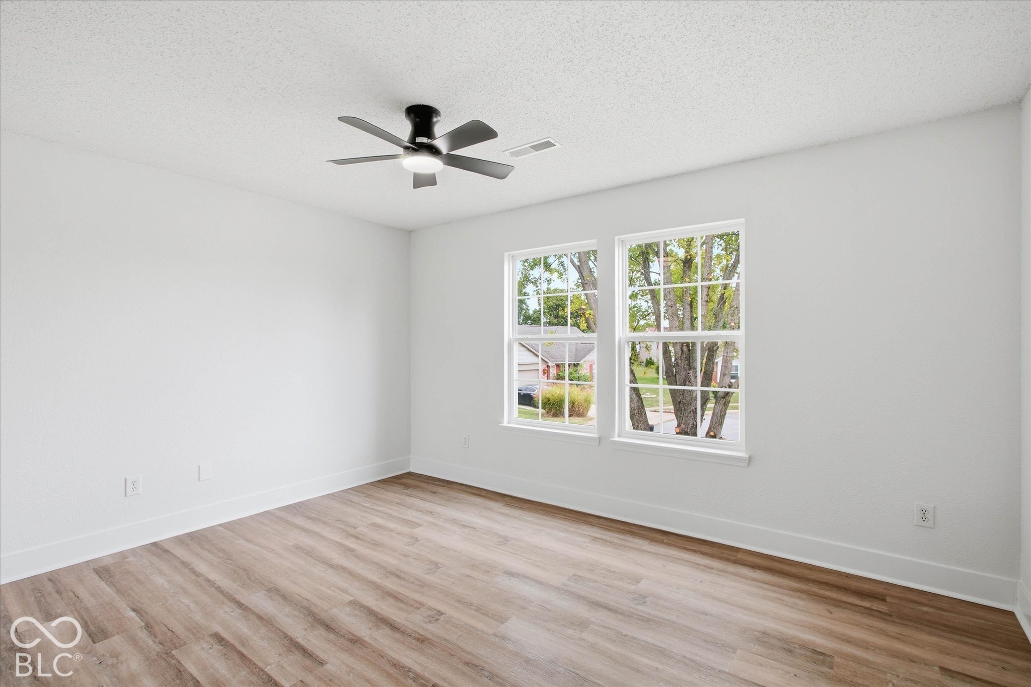 Room featuring wood-finish flooring, dual windows with white trim, and a matte black ceiling fan with integrated lighting