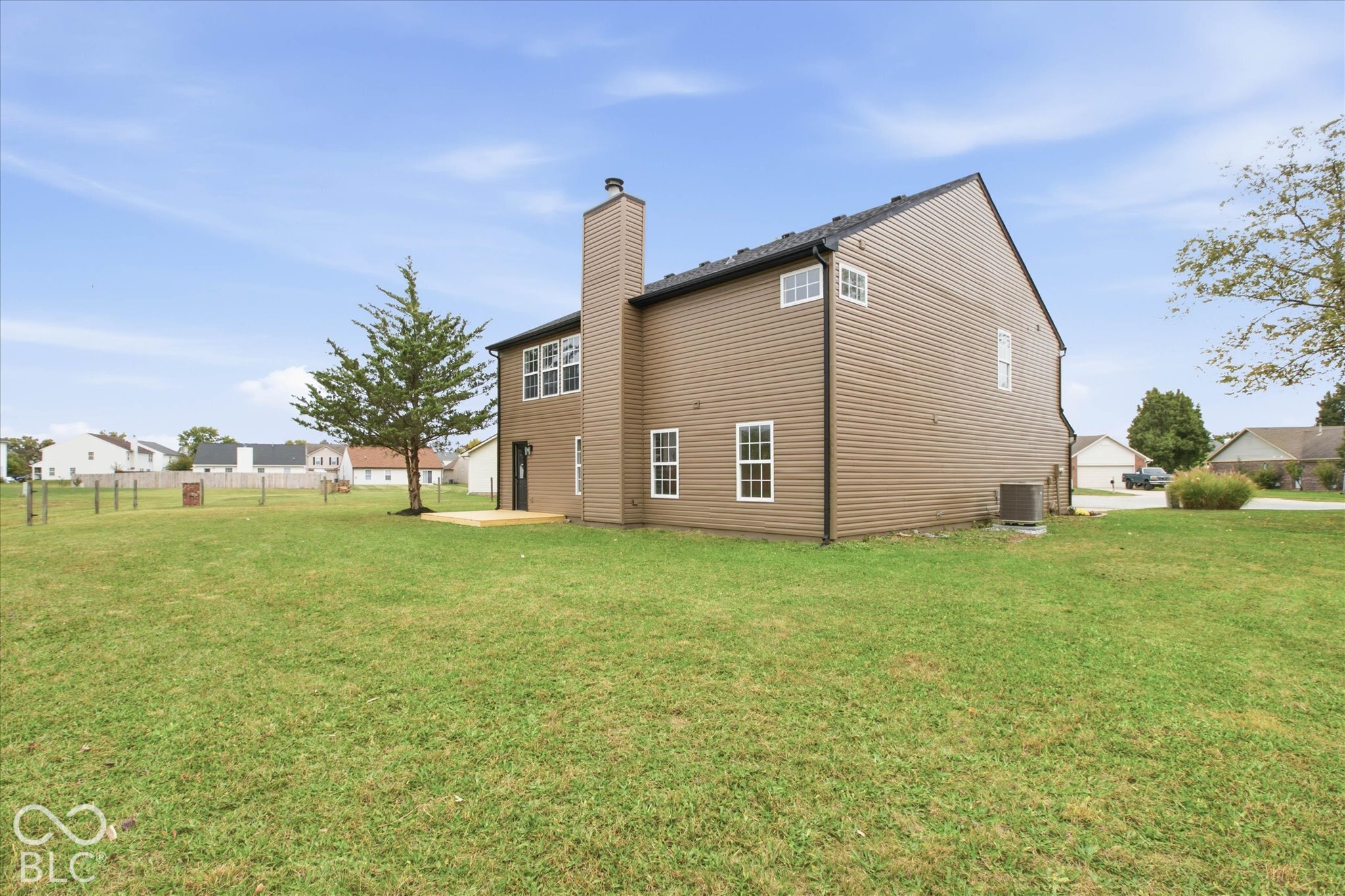 Two-story home with brown horizontal siding, an exterior chimney, multiple grid-pattern windows, and an expansive grass yard featuring a wood deck