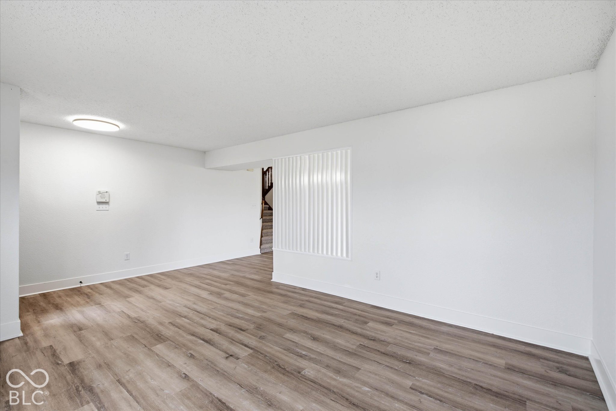 Neutral-toned interior featuring wood-finish flooring, crisp white wall finishes, and a flush-mount circular ceiling light fixture