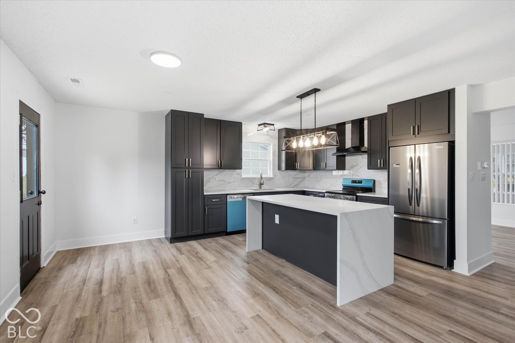Kitchen featuring charcoal cabinetry, waterfall-edge island with light-toned stone-finish countertop, stainless steel appliances, and wood-finish flooring