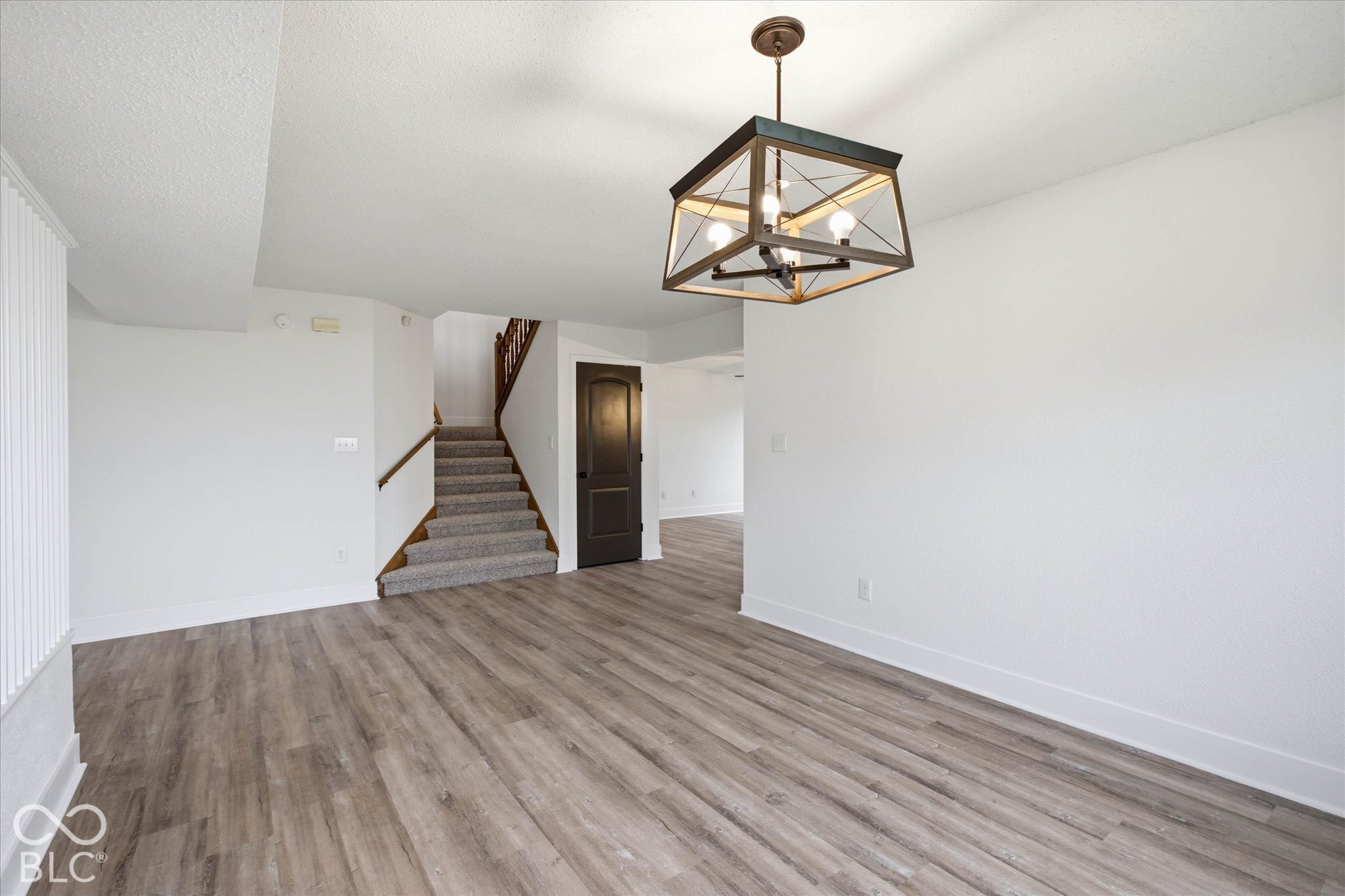 Open floor plan featuring wood-finish flooring, a geometric metal chandelier, a carpeted staircase with a wooden handrail, and a raised-panel interior door