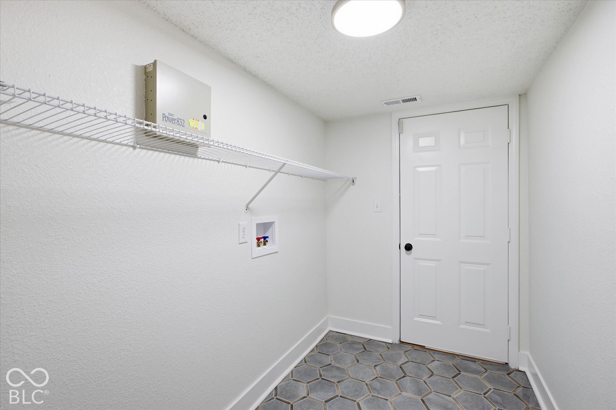 Utility area featuring hexagonal tile flooring, wall-mounted wire shelving, and recessed laundry hookups with a white six-panel interior door