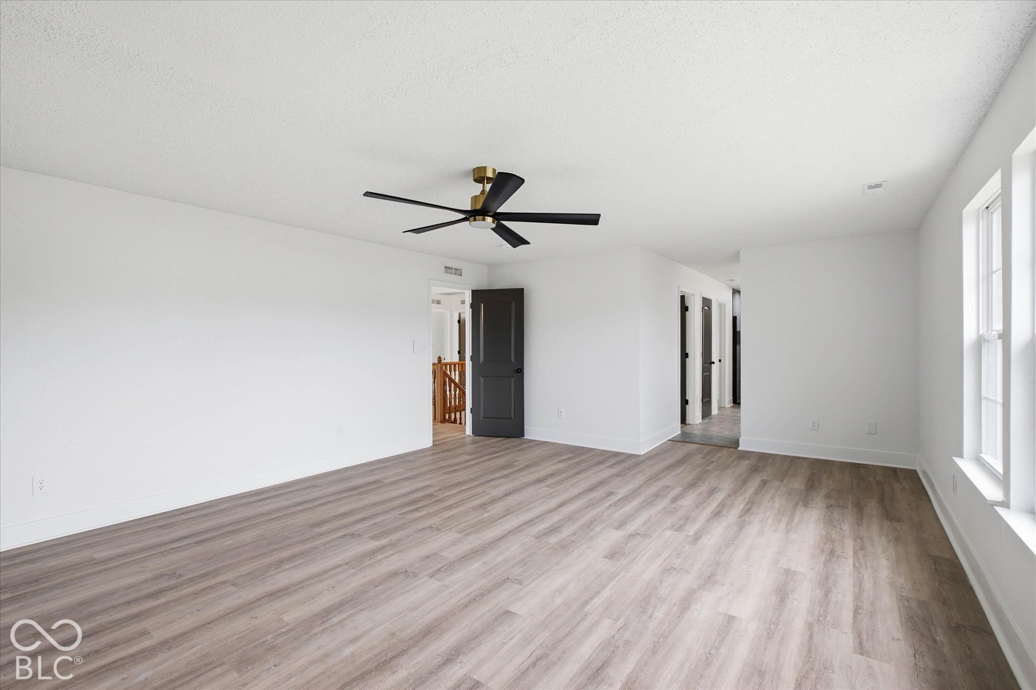 Spacious room featuring wood-finish flooring, a modern matte black ceiling fan, white walls, and contrasting matte black interior doors