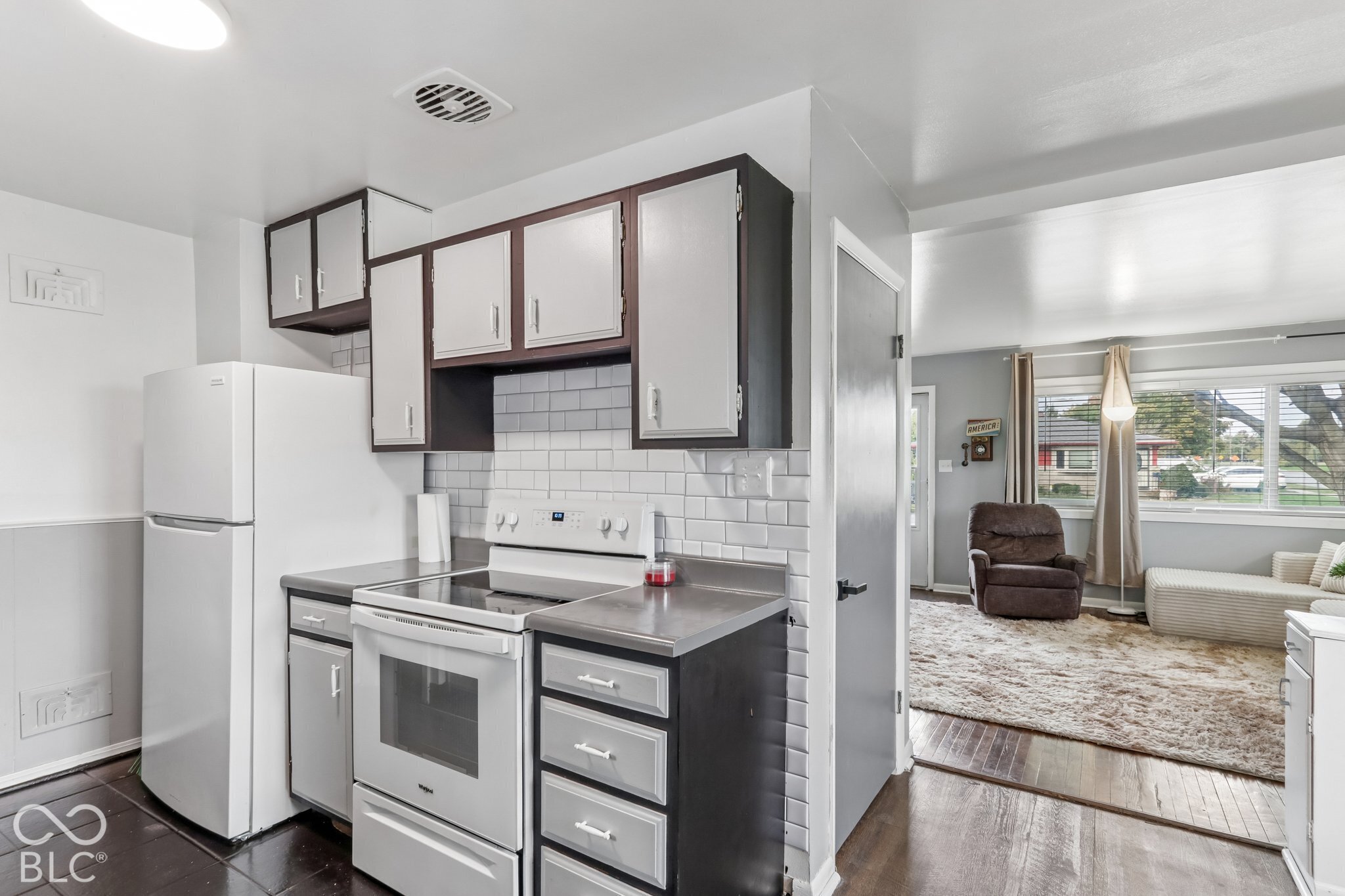 Kitchen featuring two-tone cabinetry, subway tile backsplash, solid-surface countertops, and wood-finish flooring
