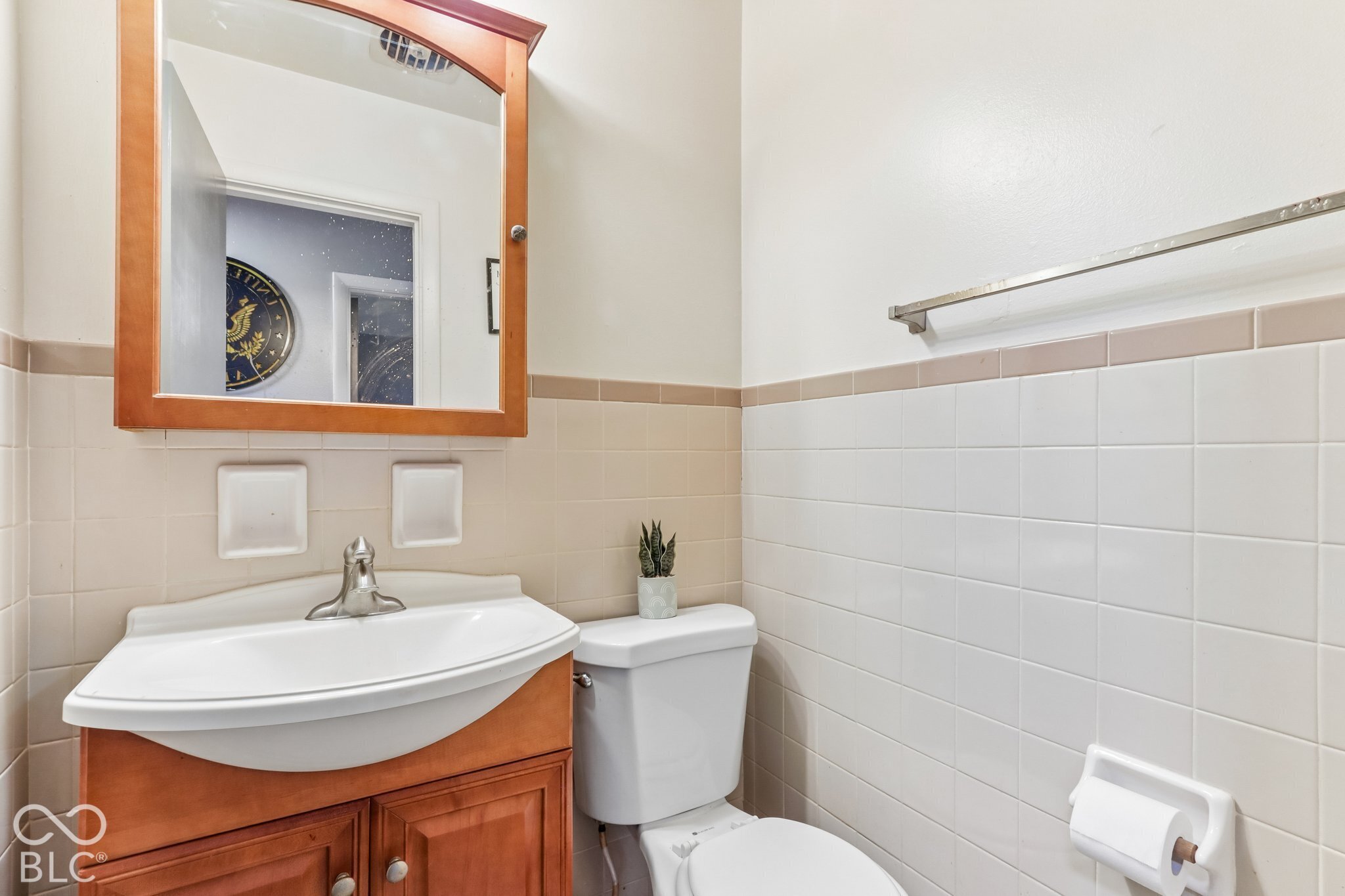 Vanity cabinet with a white molded sink, single-handle faucet, arched medicine cabinet, and ceramic wall tile wainscoting