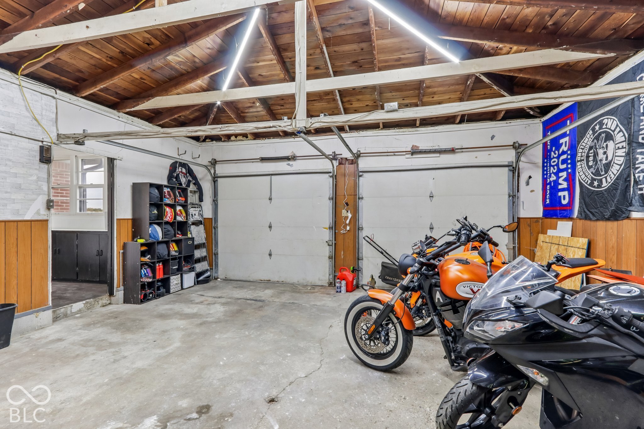 Two-car garage featuring exposed wood beam ceiling, concrete flooring, and linear LED lighting