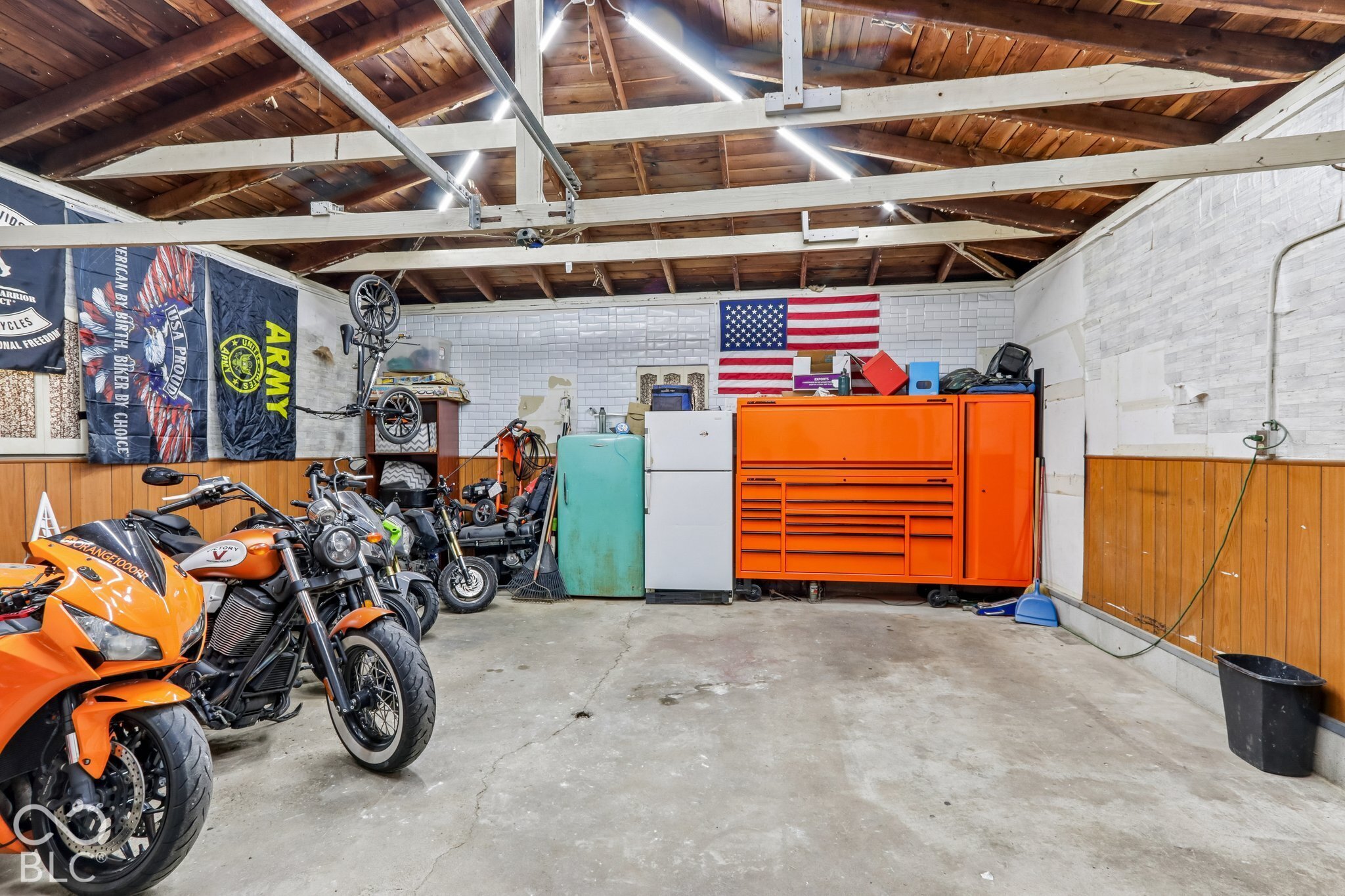 Detached garage space featuring an exposed wood-beam ceiling, concrete flooring, and tiled wall accents