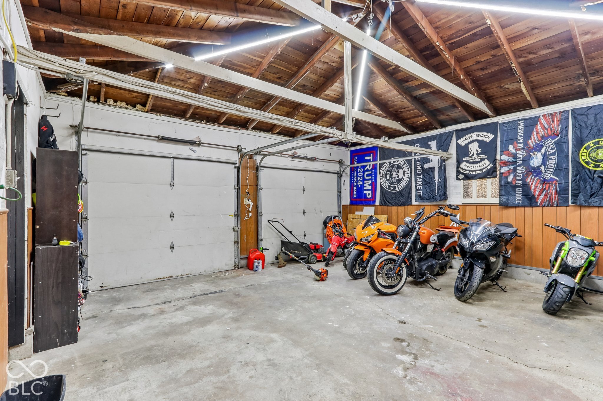 Multi-car garage featuring exposed wood rafters, concrete flooring, dual metal overhead doors, and wood-paneled walls