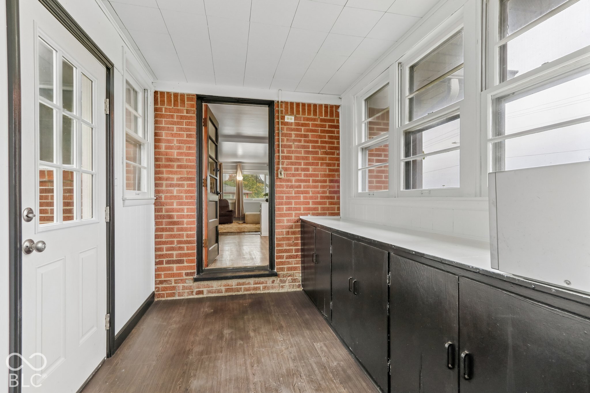 Enclosed sunroom featuring exposed brick walls, wood-finish flooring, built-in lower cabinetry with a continuous surface, and multiple windows