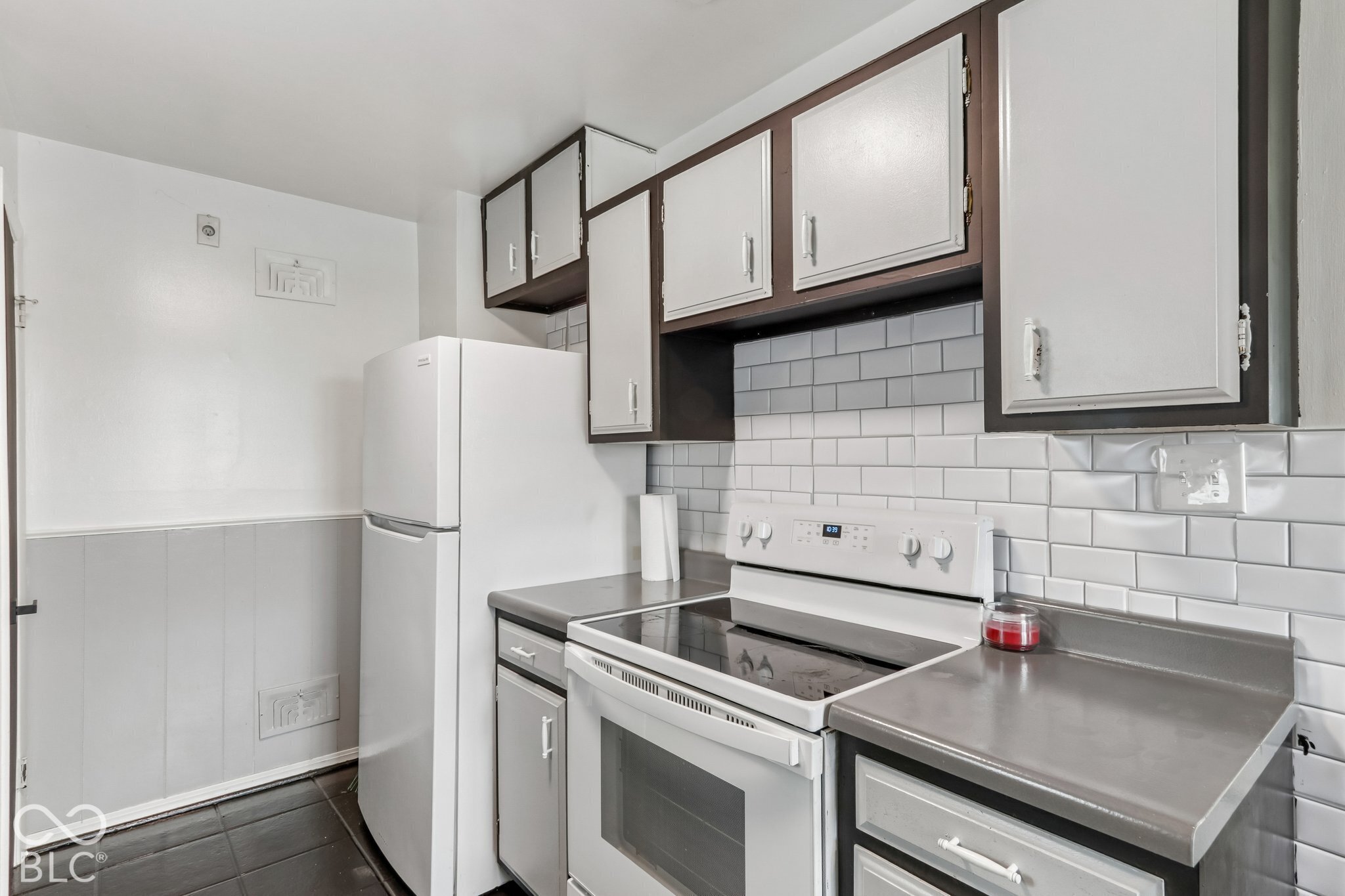 Kitchen featuring white subway tile backsplash, solid-surface countertops, two-toned cabinetry, and white appliances