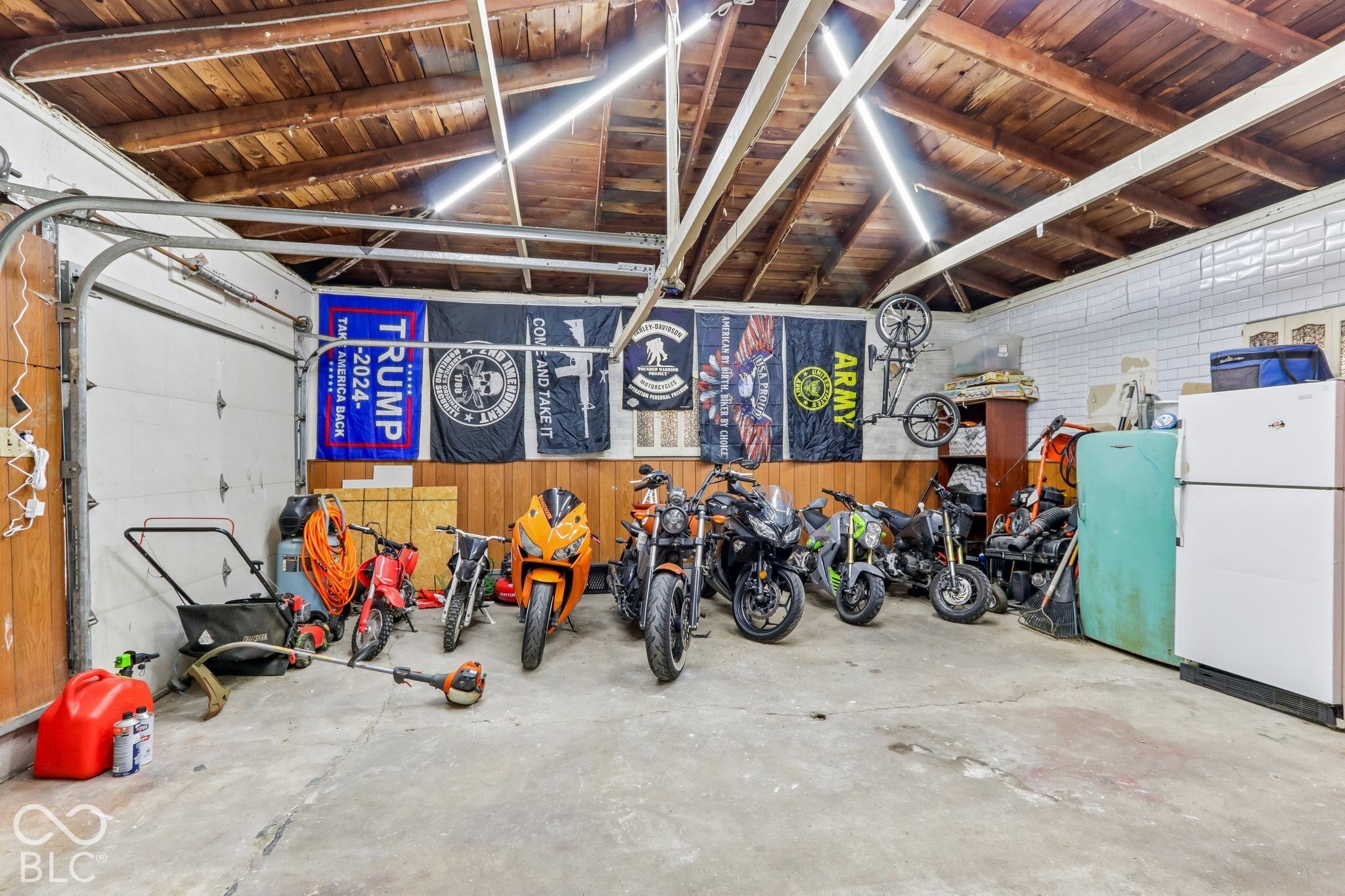 Enclosed garage featuring exposed wood ceiling rafters, concrete flooring, wood paneled walls, and built-in white wall tiling