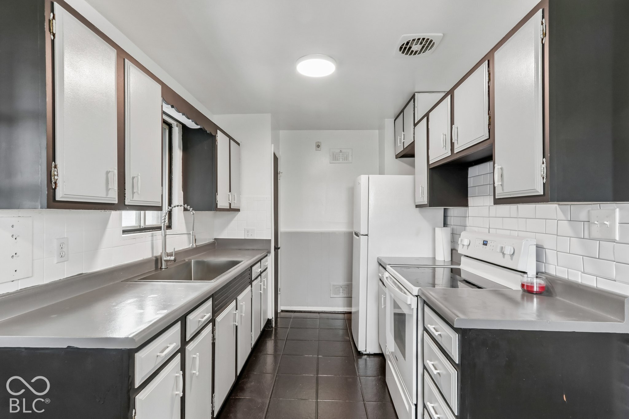 Kitchen featuring white subway tile backsplash, dark cabinetry with white panels, solid surface countertops, stainless steel undermount sink with arched pull-down faucet, and tiled flooring