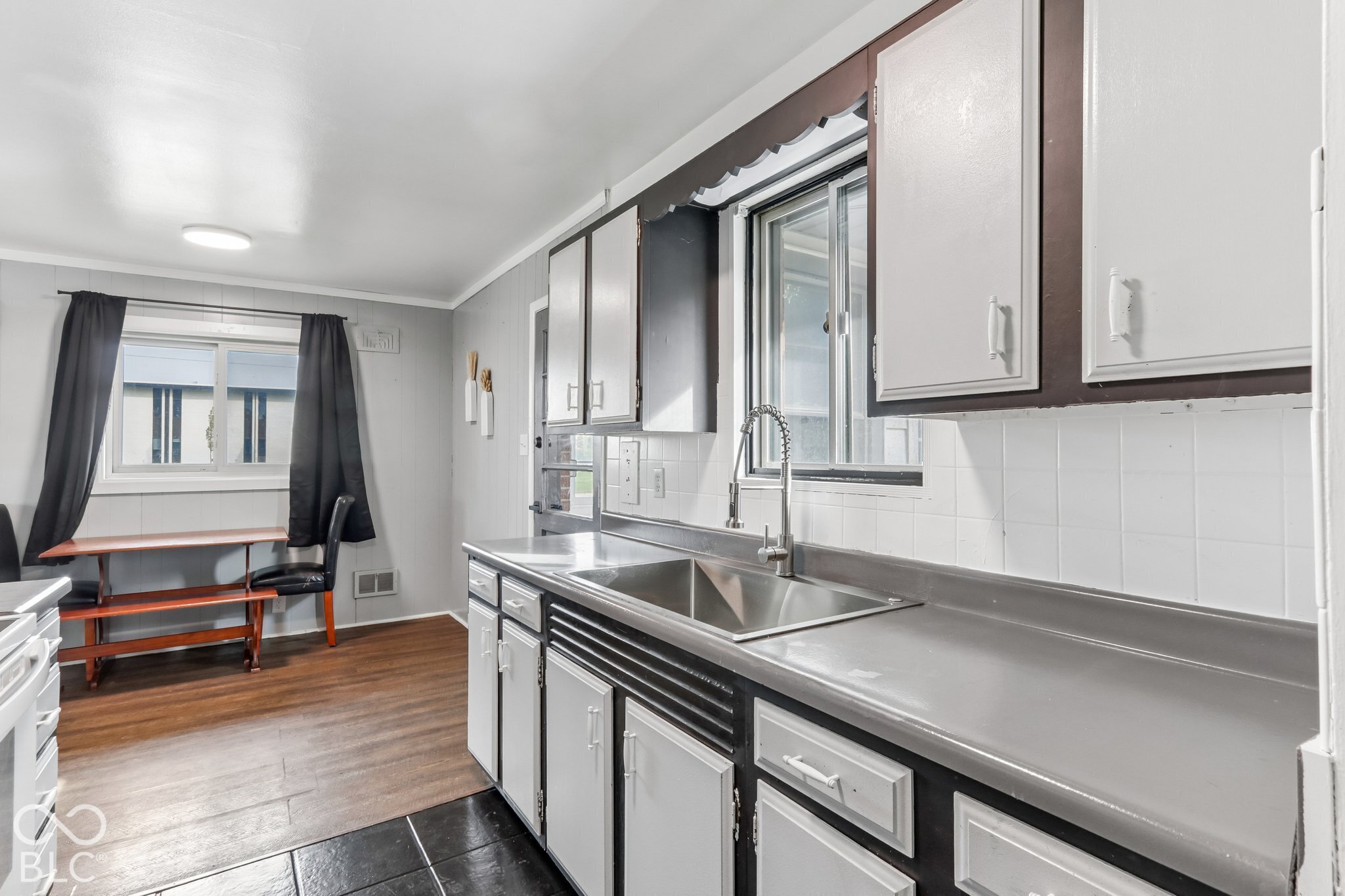 Kitchen featuring wood-finish flooring, shaker-style cabinetry with contrasting trim, a stainless steel undermount sink, a gooseneck faucet, and a tiled backsplash