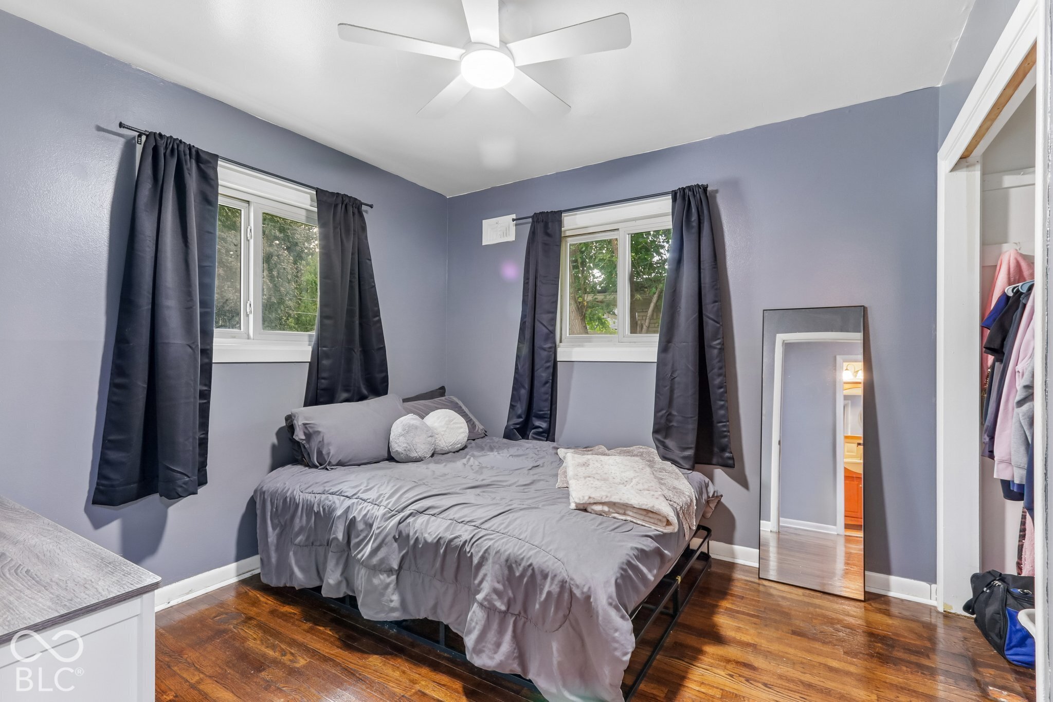 Room featuring dark-stained wood-finish flooring, dual windows with white frames, and a multi-blade ceiling fan with integrated lighting