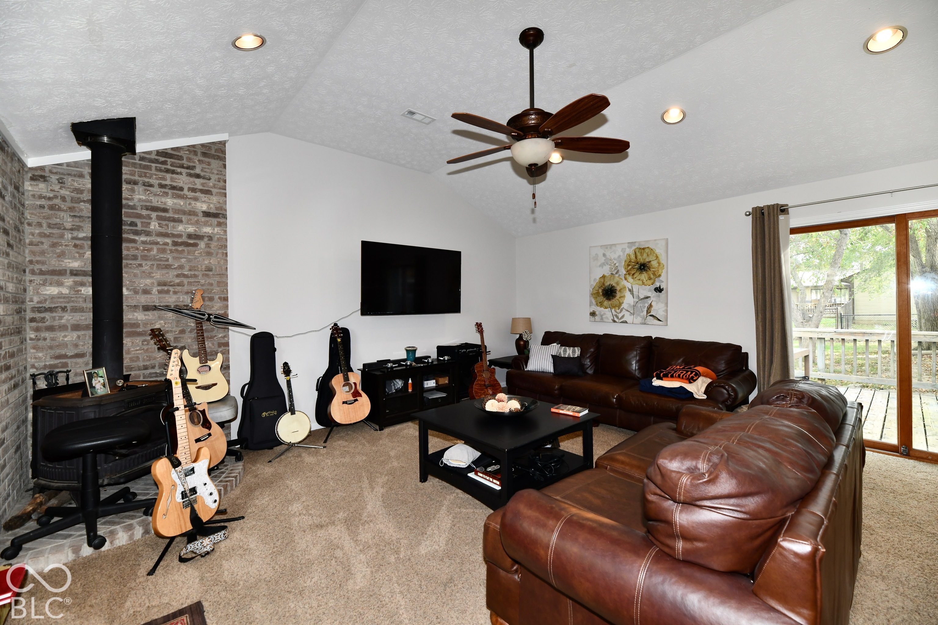 Vaulted ceilings featuring recessed lighting and a ceiling fan, exposed brick fireplace with a wood-burning stove, and a sliding glass door