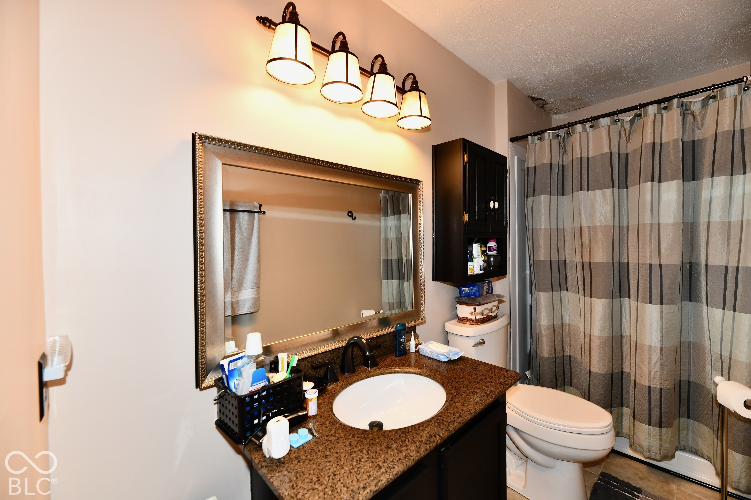 Bathroom vanity featuring a dark-finish base cabinet, stone-composite countertop with an integrated oval basin, wall-mounted four-light fixture, and framed vanity mirror with built-in wall cabinetry