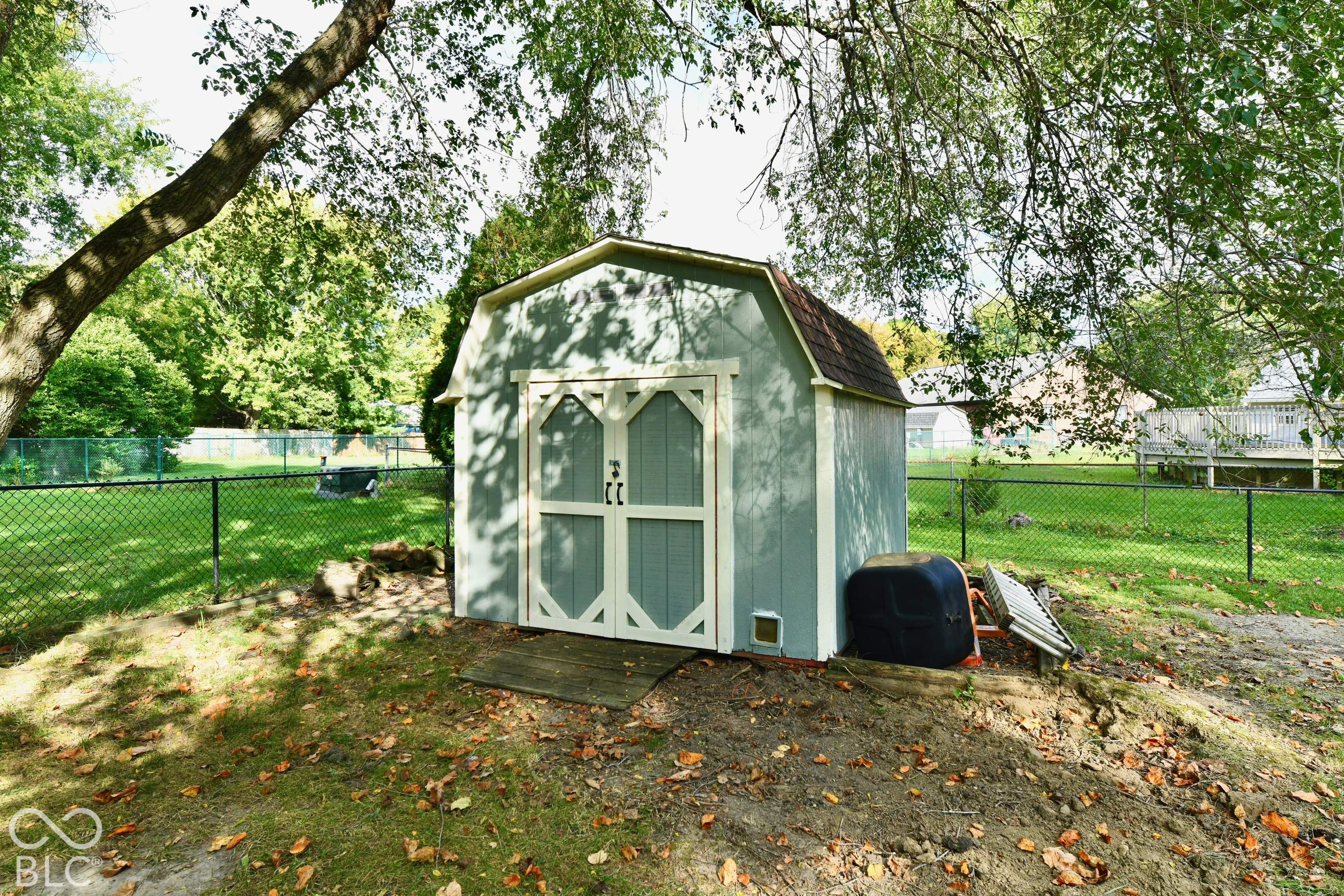 Barn-style exterior storage shed featuring double doors, shingled roofing, and a fenced backyard