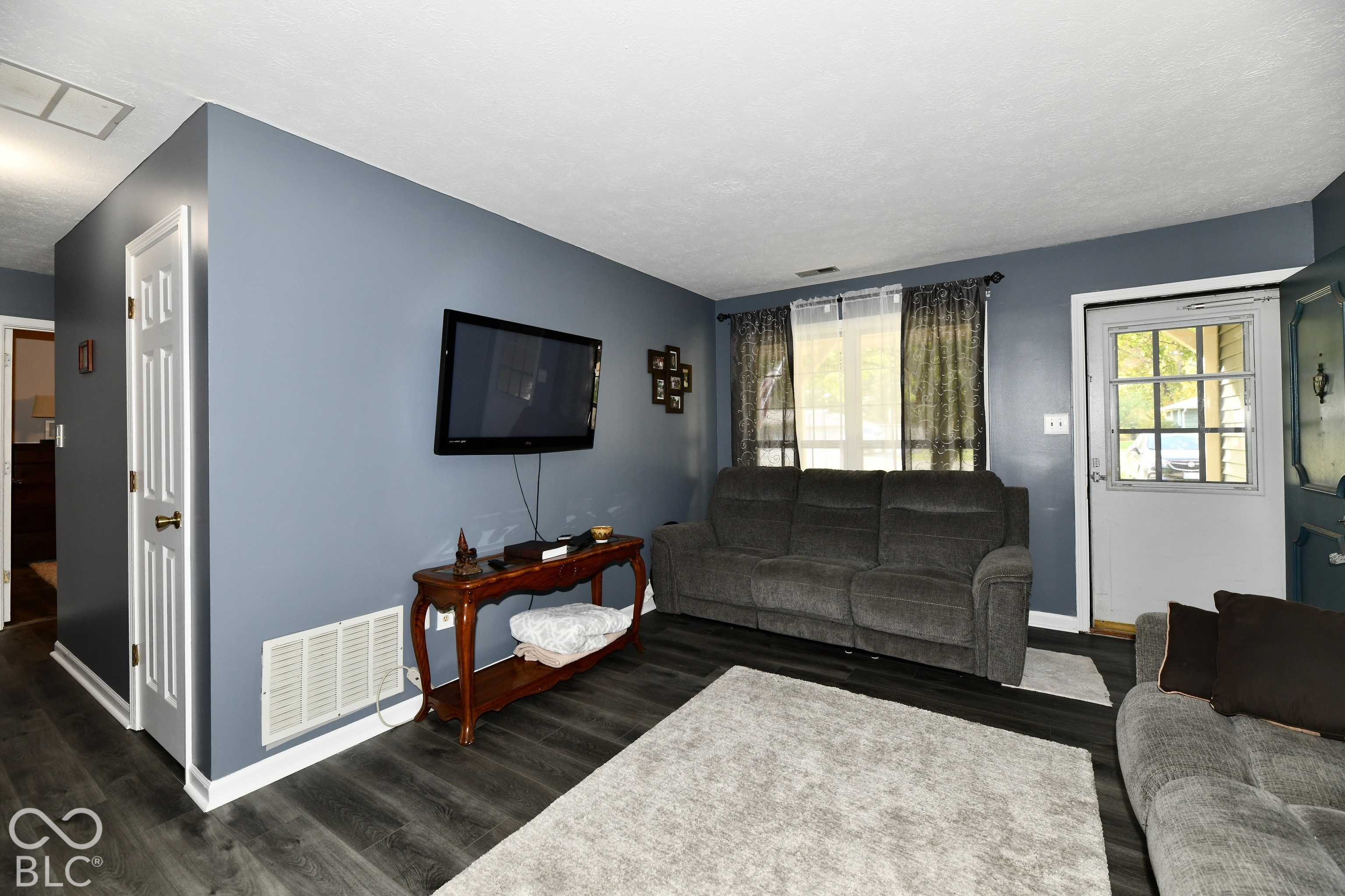 Living area featuring wood-finish flooring, a multi-pane glass entry door, and large window with dark trim