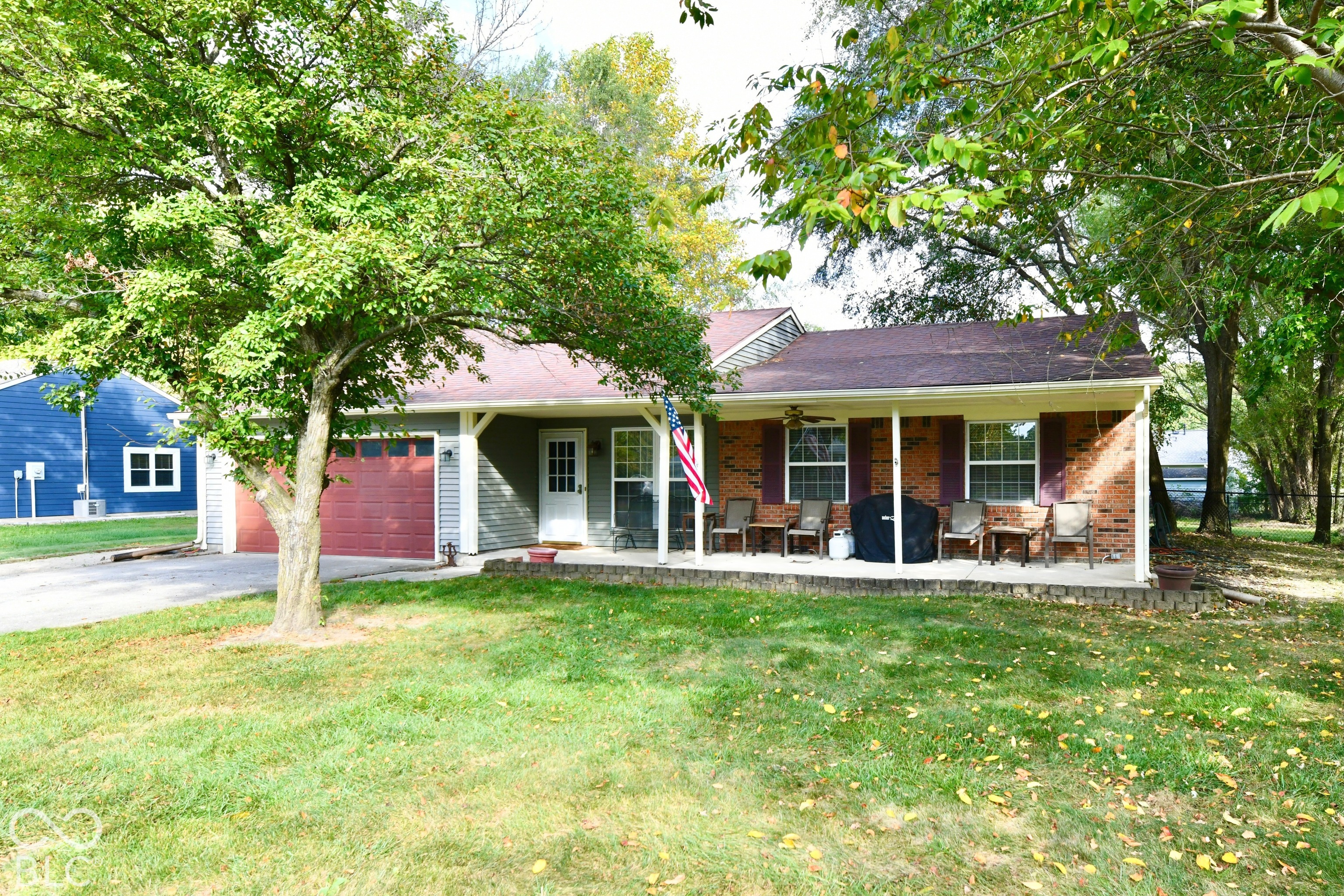 Ranch-style exterior featuring a mix of brick and horizontal siding, a covered front porch with support pillars, an attached garage with a carriage-style door, and mature landscaping