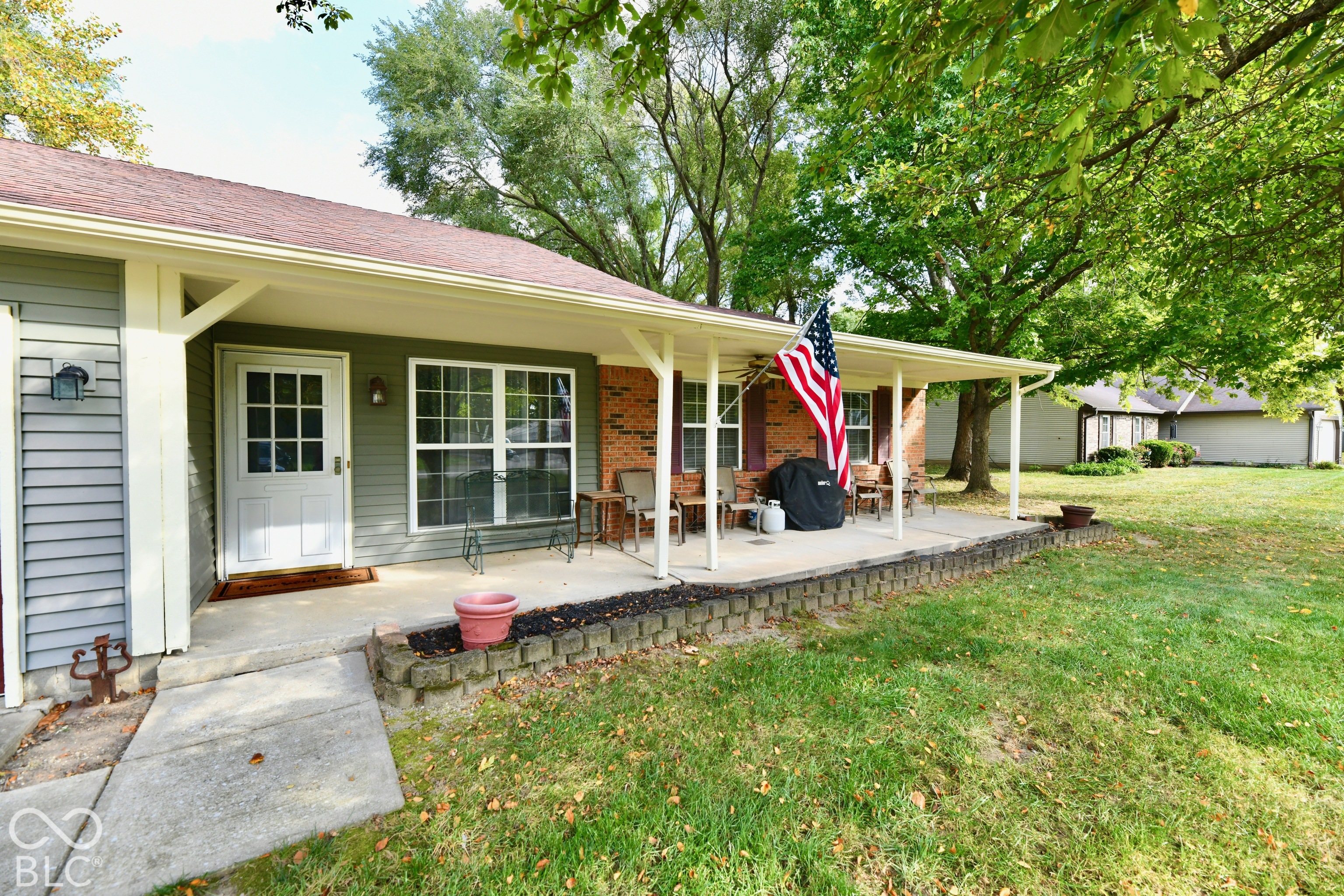 Covered front porch featuring a concrete patio, brick exterior accents, siding, and a segmented block landscape border