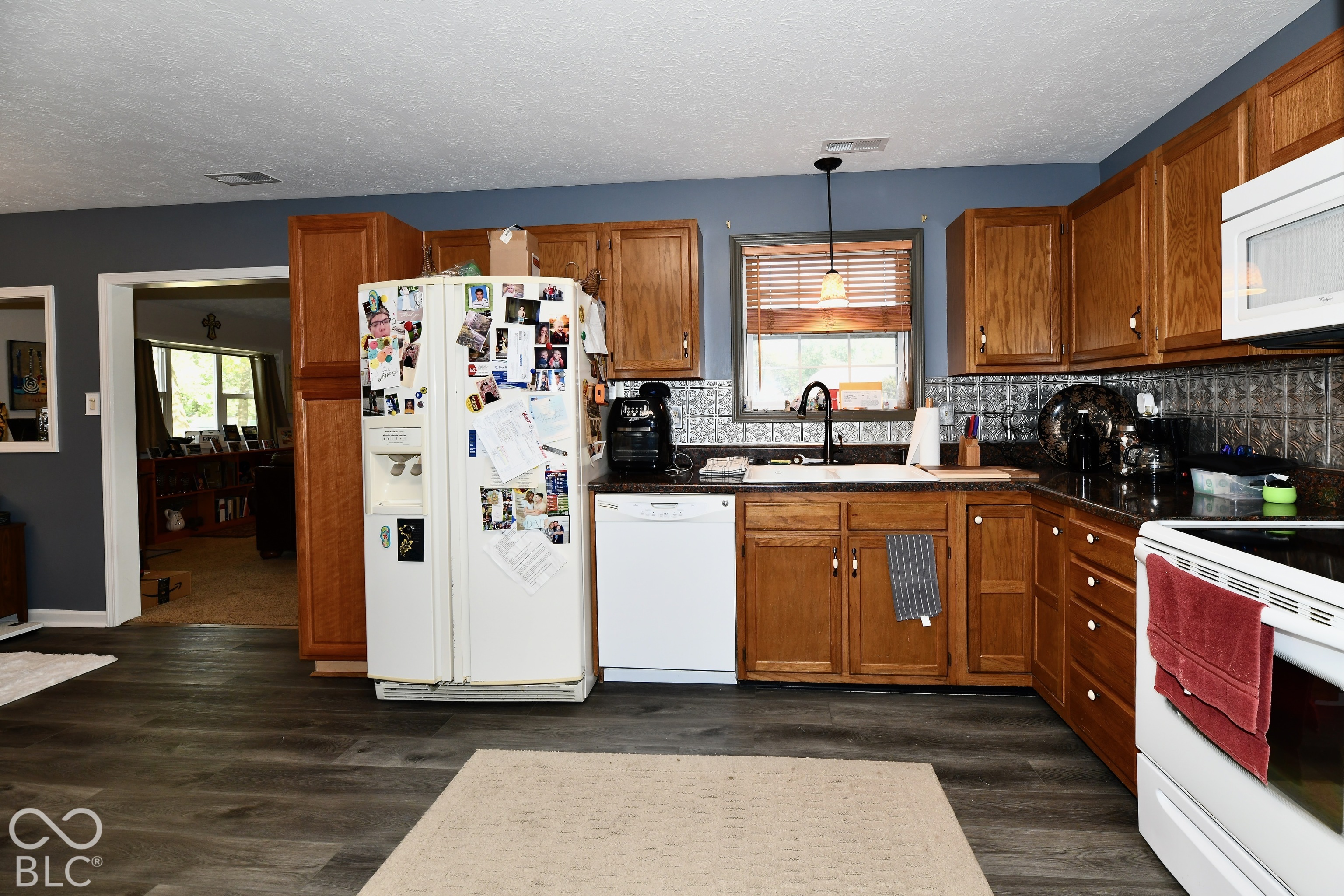 Kitchen featuring wood cabinetry, patterned tile backsplash, wood-finish flooring, dark stone countertops, and a white farmhouse-style sink with a matte black faucet