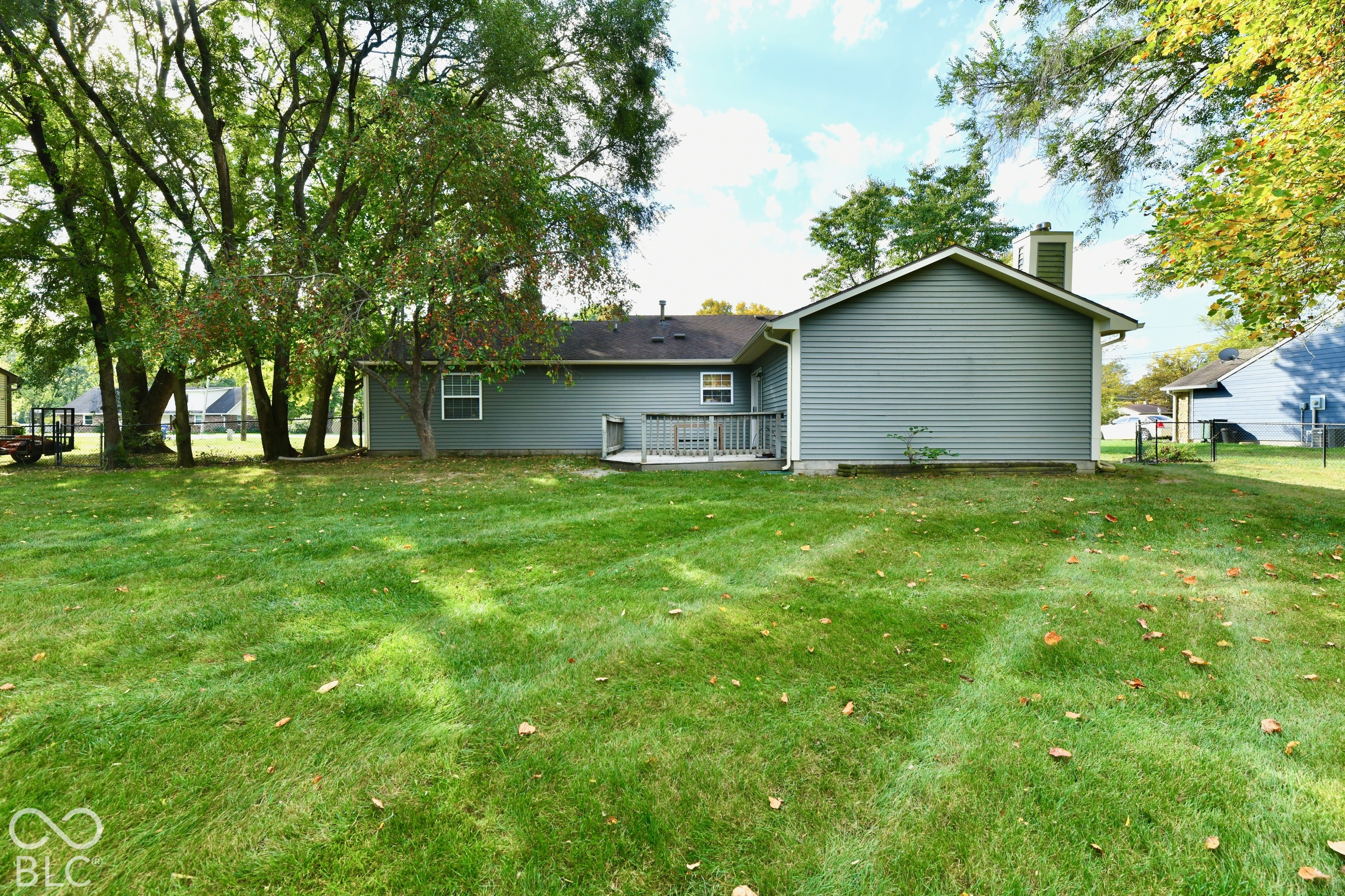 Expansive backyard featuring a sprawling lawn, mature trees, exterior horizontal siding, a chimney, and a raised wooden deck