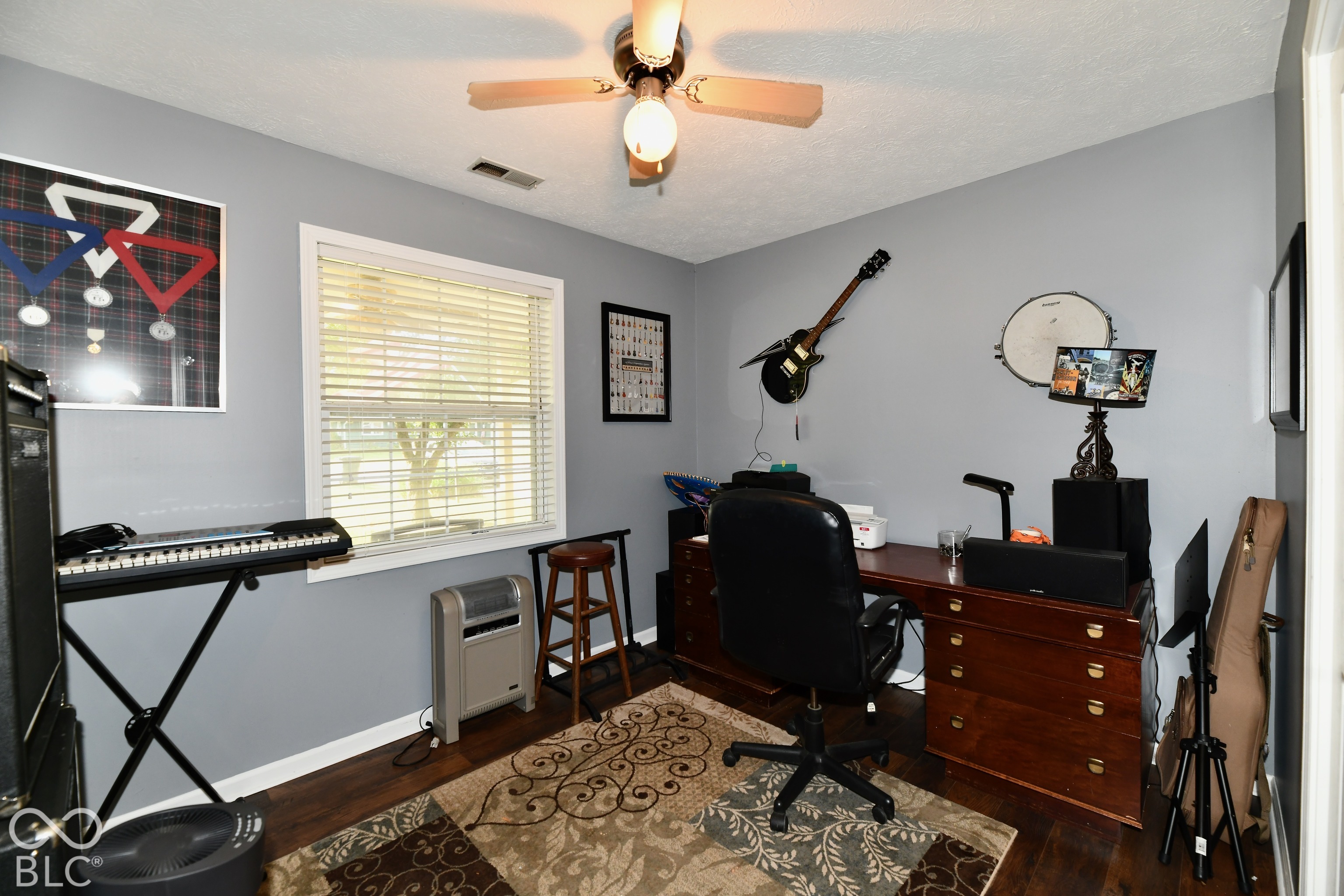 Room featuring wood-finish flooring, a multi-blade ceiling fan with integrated lighting, and a window with horizontal blinds