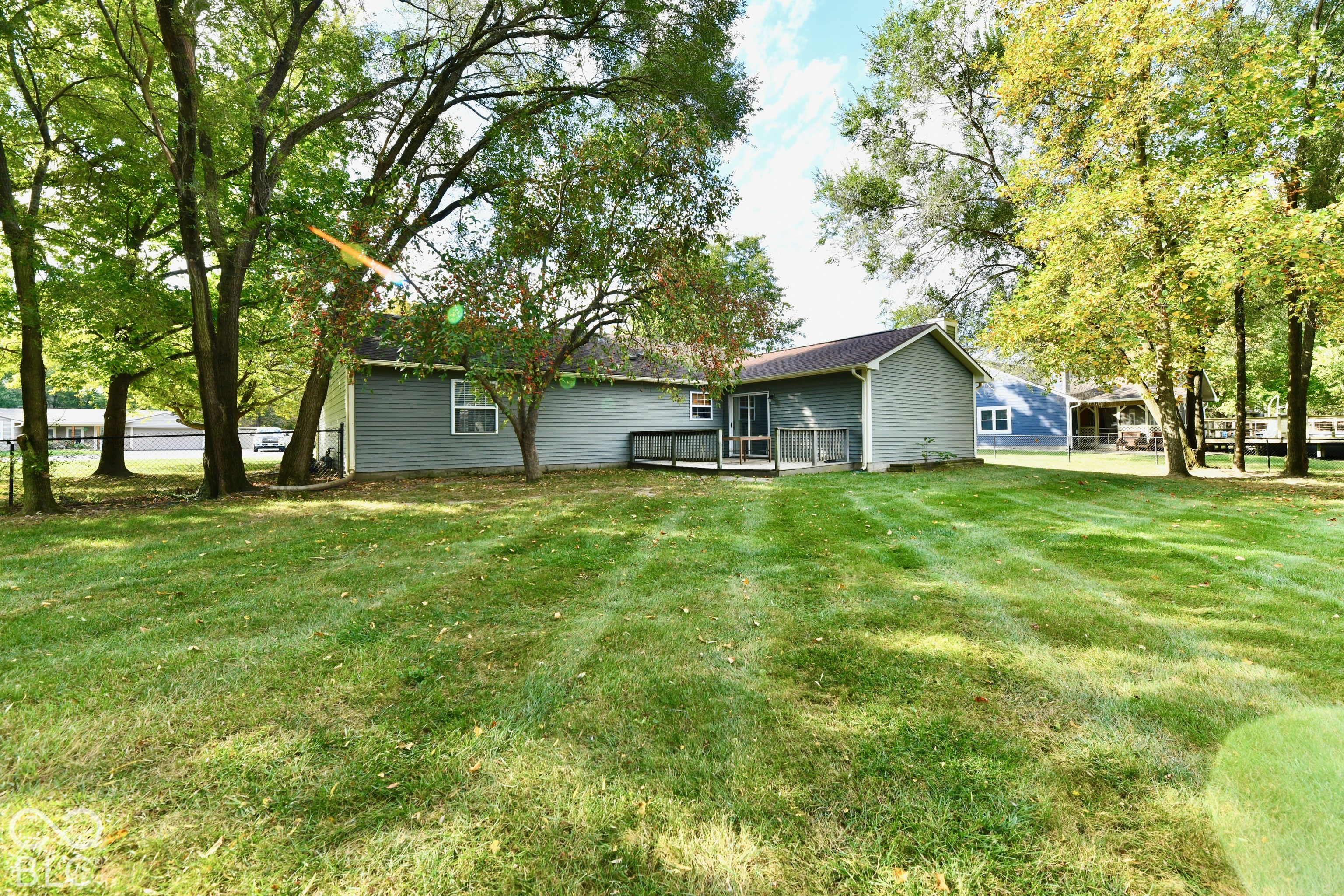 Expansive backyard featuring a large grass lawn, mature trees, and a wooden deck