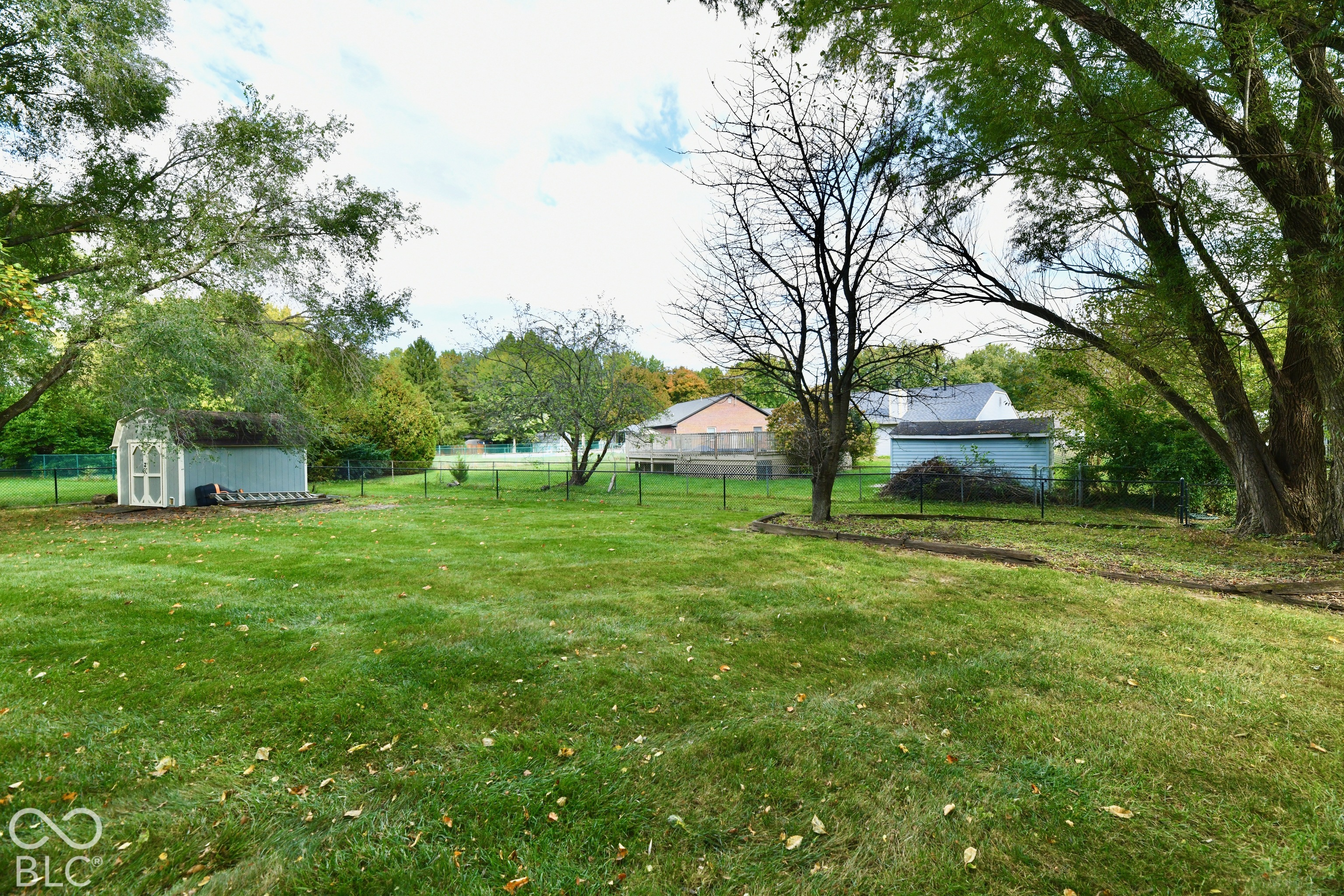 Expansive backyard featuring a large grass lawn, mature trees, perimeter fencing, and two detached storage structures