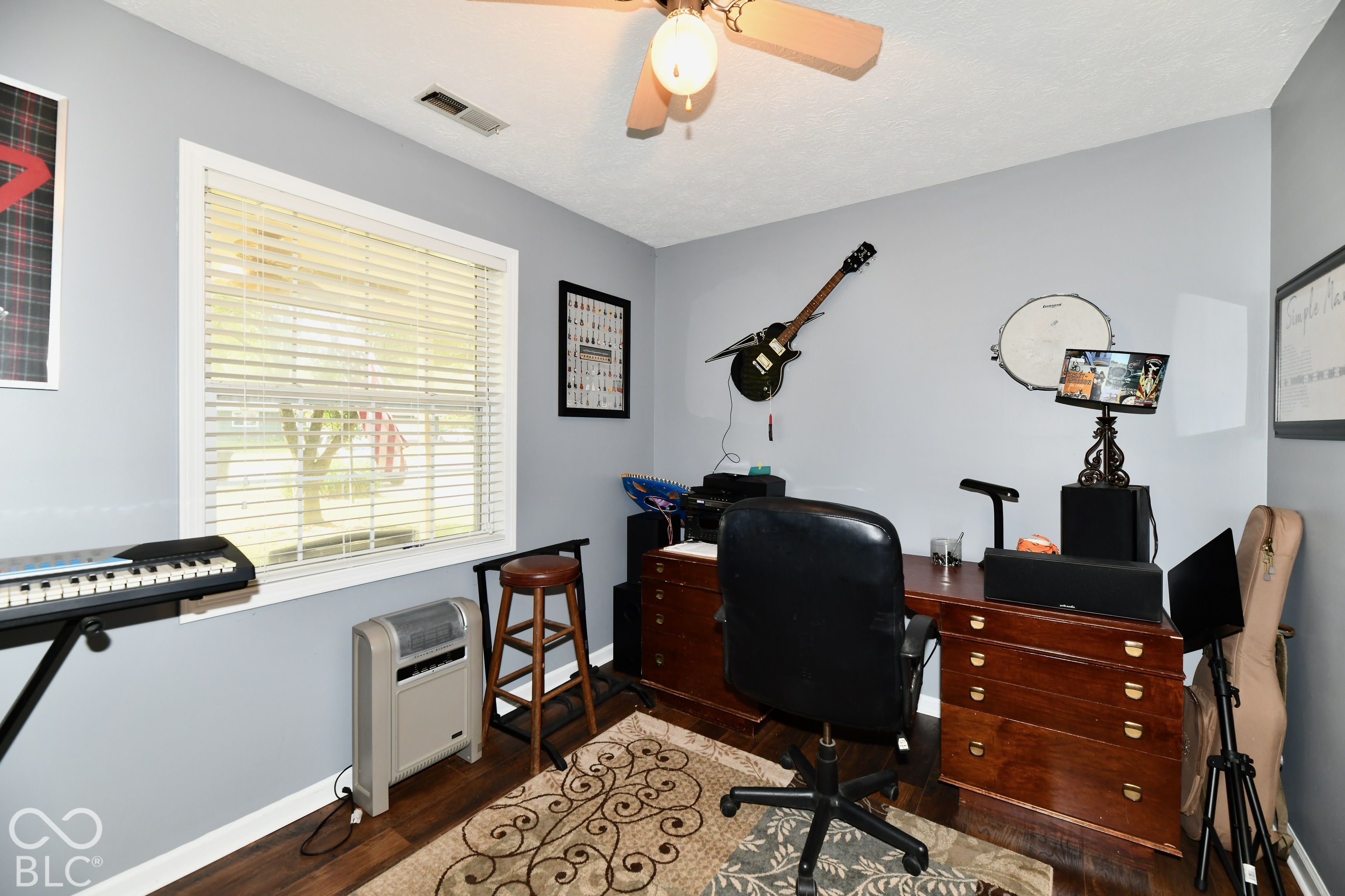 Neutral wall palette, wood-finish flooring, multi-pane window with horizontal blinds, and a ceiling-mounted light fixture with fan