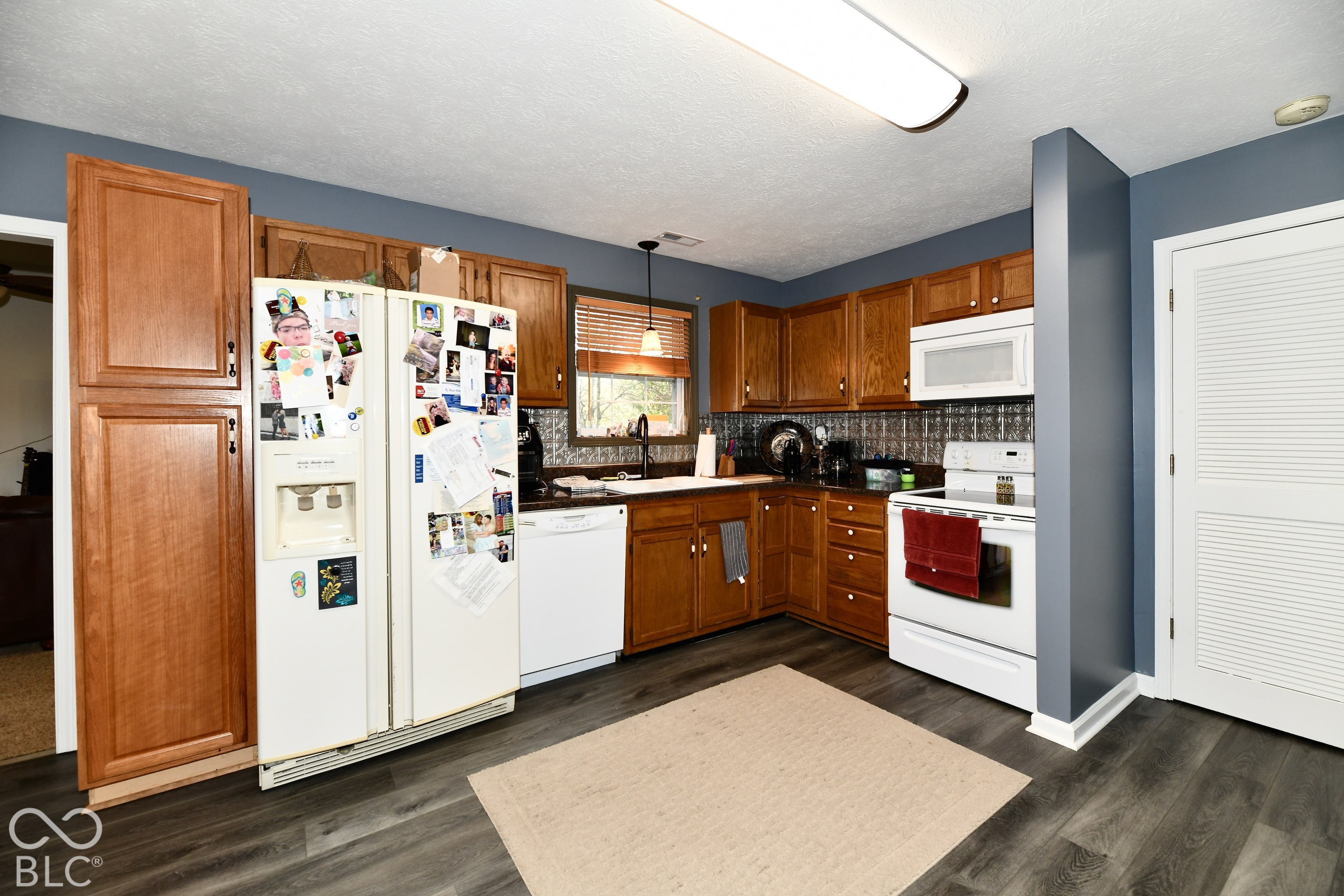 Kitchen featuring wood cabinetry, dark-toned wood-finish flooring, a white undermount sink with a matte black faucet, and a metallic-finish backsplash