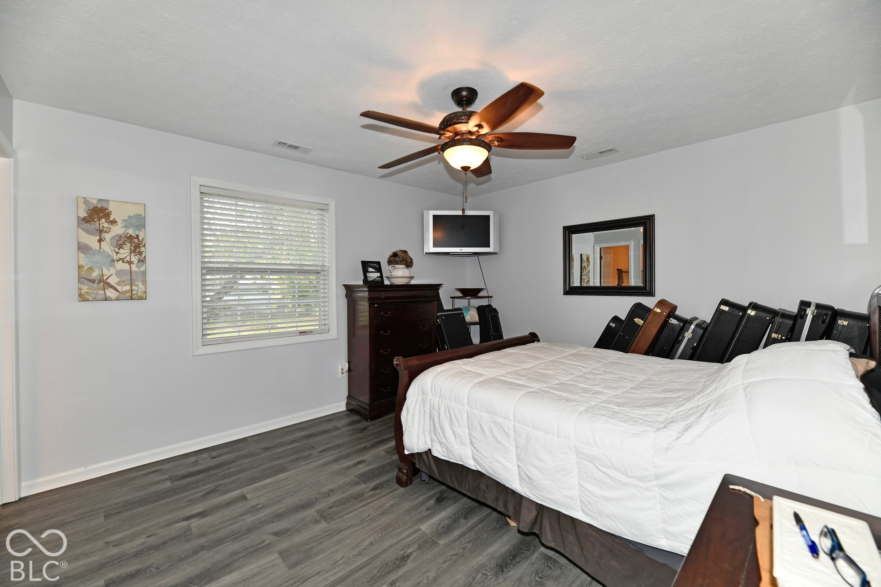 Interior space featuring wood-finish flooring, a ceiling fan with integrated light fixture, and a window with horizontal blinds