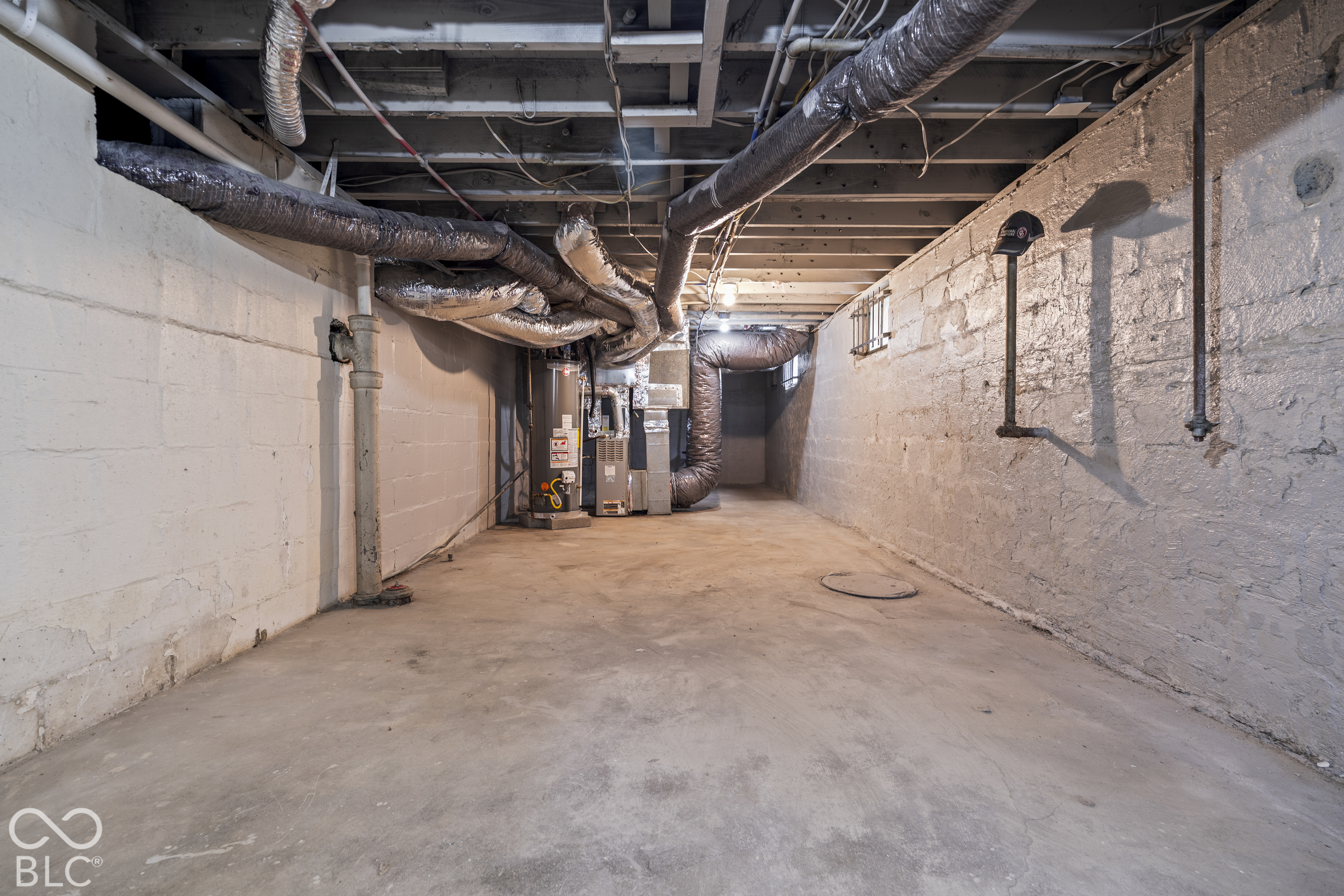 Unfinished basement area featuring exposed ceiling joists, painted concrete block walls, concrete flooring, and an installed water heater and furnace system