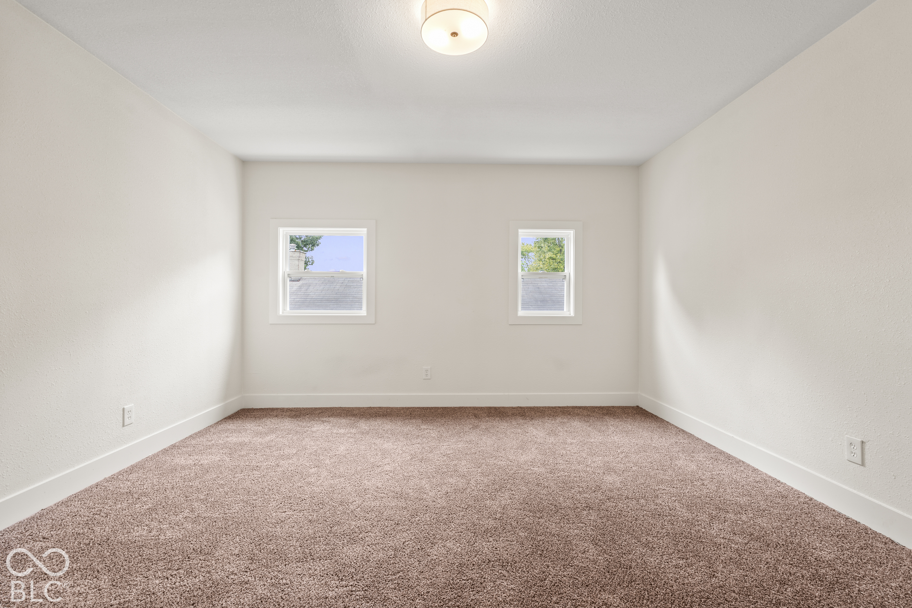 Neutral-toned interior space featuring wall-to-wall carpeting, dual windows with white casing, and a centered flush-mount light fixture
