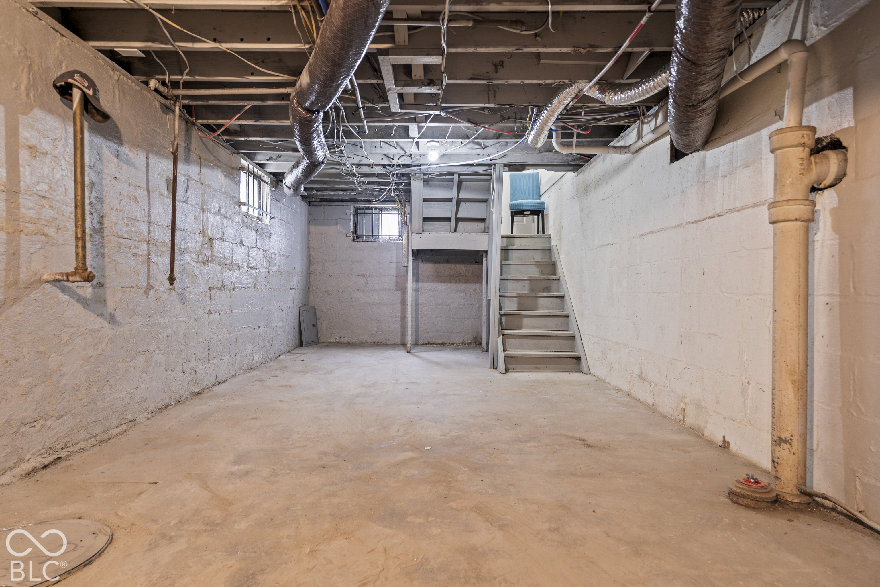 Unfinished lower level with concrete flooring, painted masonry walls, exposed ceiling joists, and small operational windows