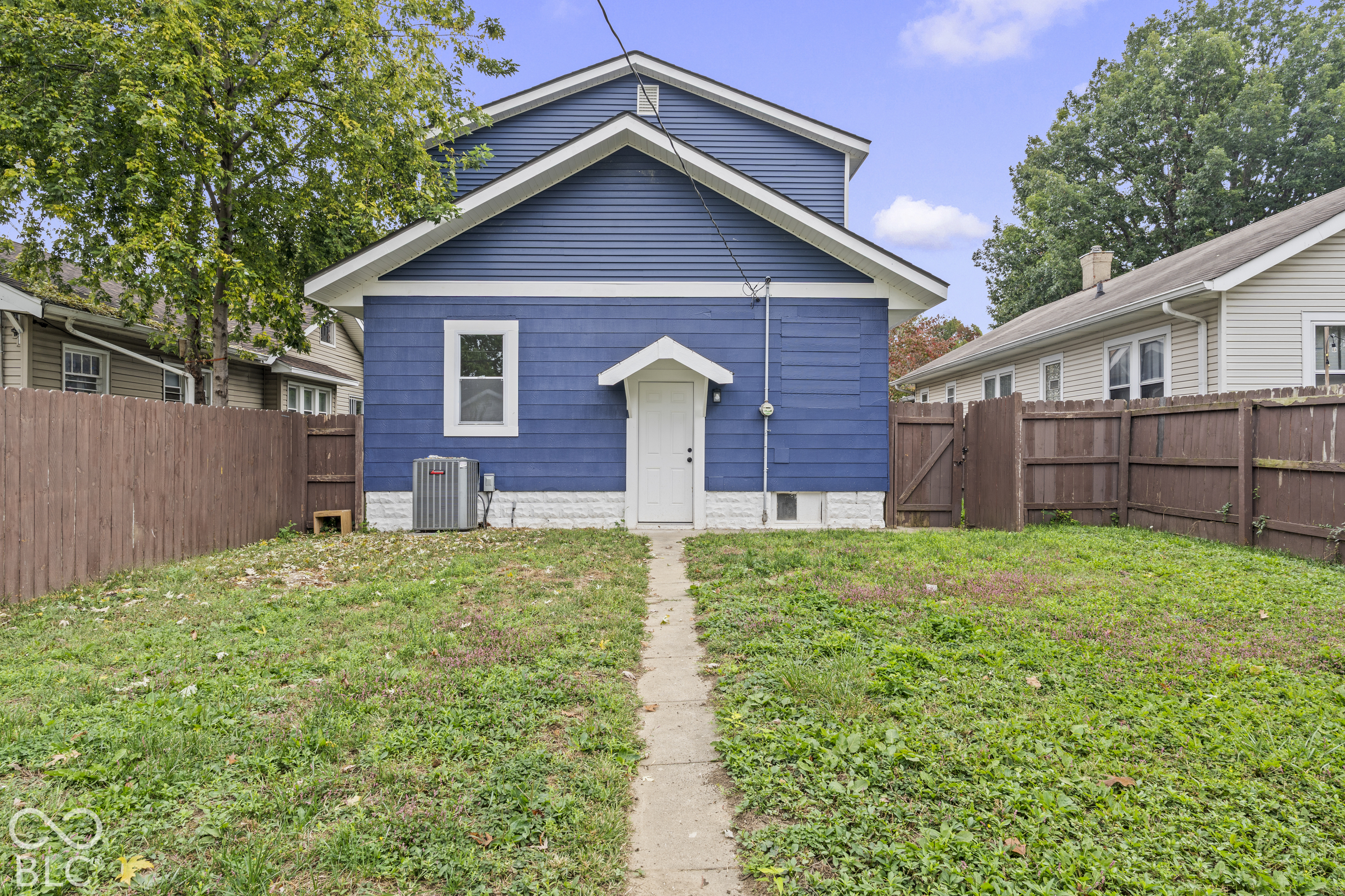 Exterior rear view featuring blue horizontal siding, white trim accents, a concrete walkway, and wood perimeter fencing Exterior rear view featuring blue horizontal siding, white trim accents, a concrete walkway, and wood perimeter fencing