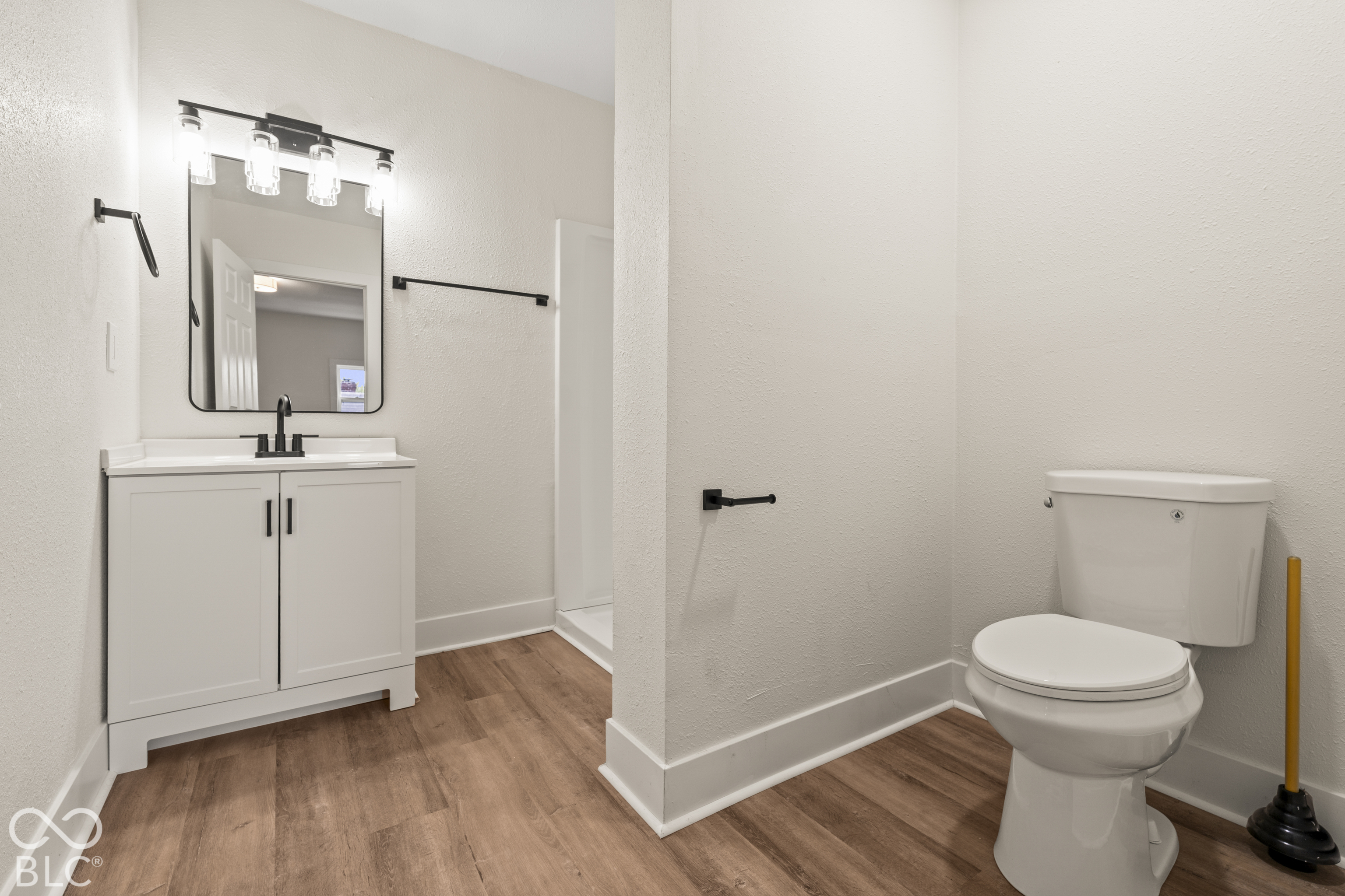 Bathroom featuring a white vanity cabinet, rectangular mirror, wood-finish flooring, four-light vanity fixture, and matte black hardware