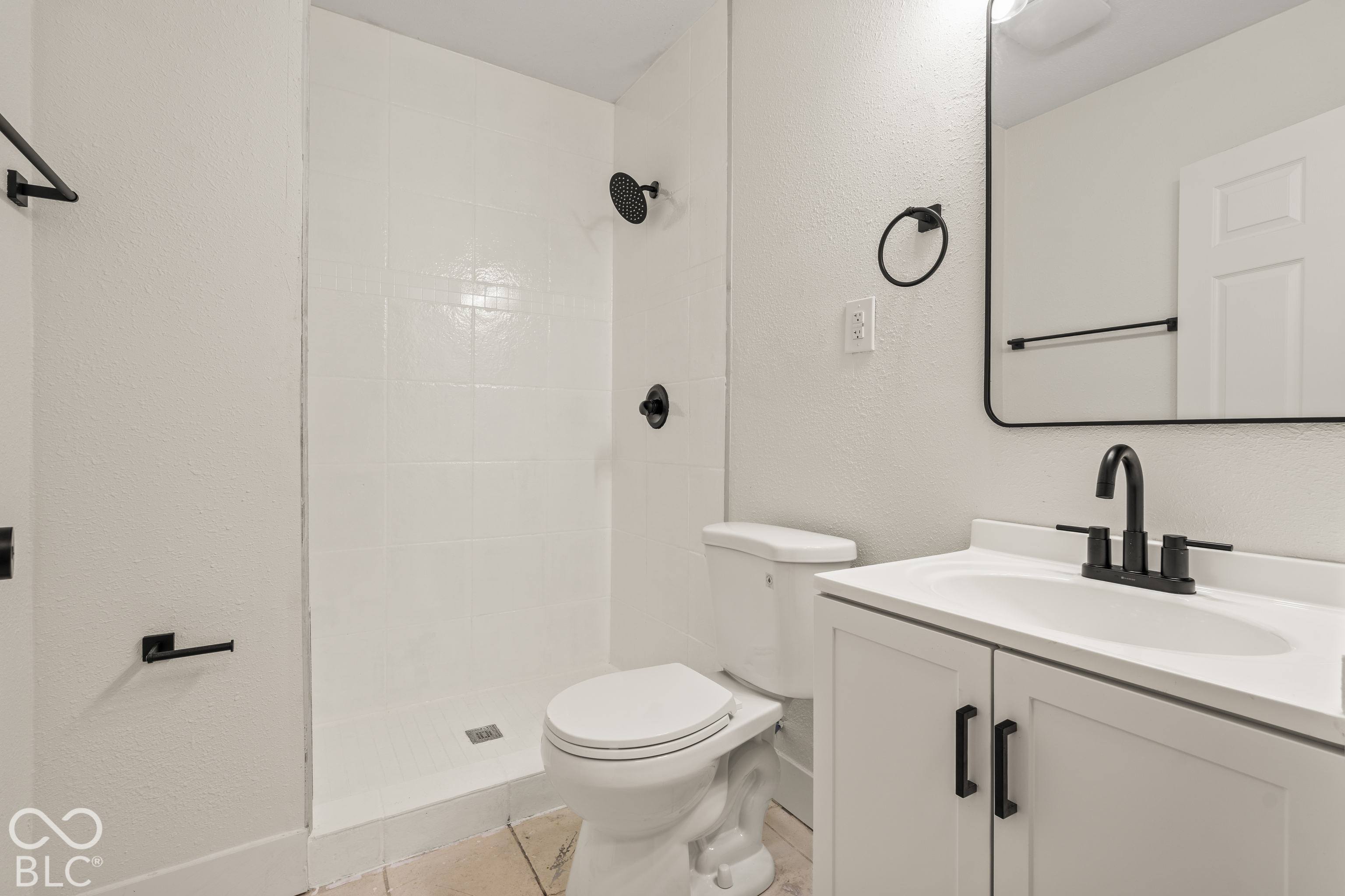 Bathroom featuring a white vanity cabinet with matte black hardware, a rectangular sink with a matte black faucet, a walk-in shower with matte black fixtures, and a rectangular mirror with a black frame