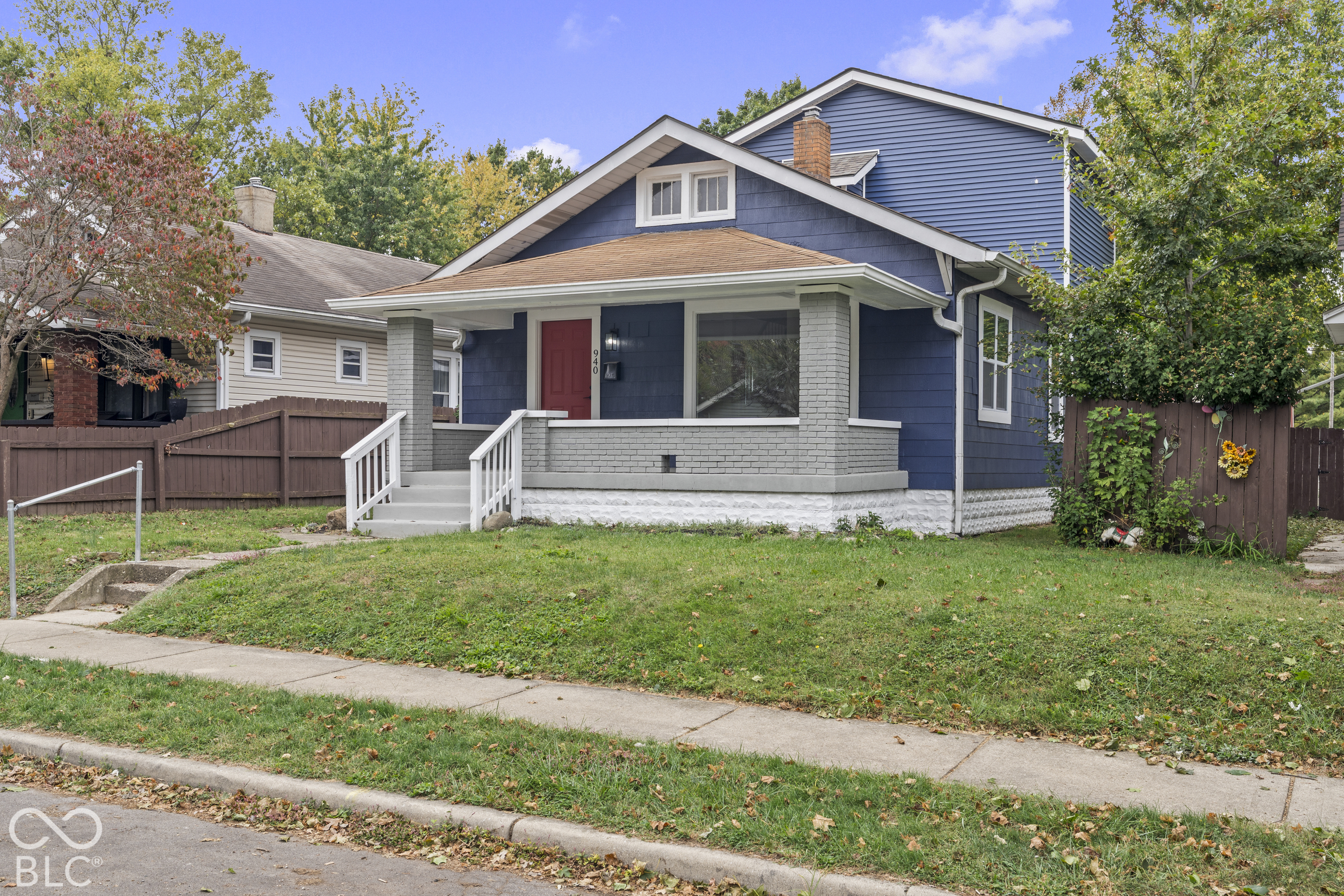 Craftsman-style exterior featuring blue horizontal siding, a covered front porch with painted brick columns, a prominent chimney, and wooden fencing Craftsman-style exterior featuring blue horizontal siding, a covered front porch with painted brick columns, a prominent chimney, and wooden fencing