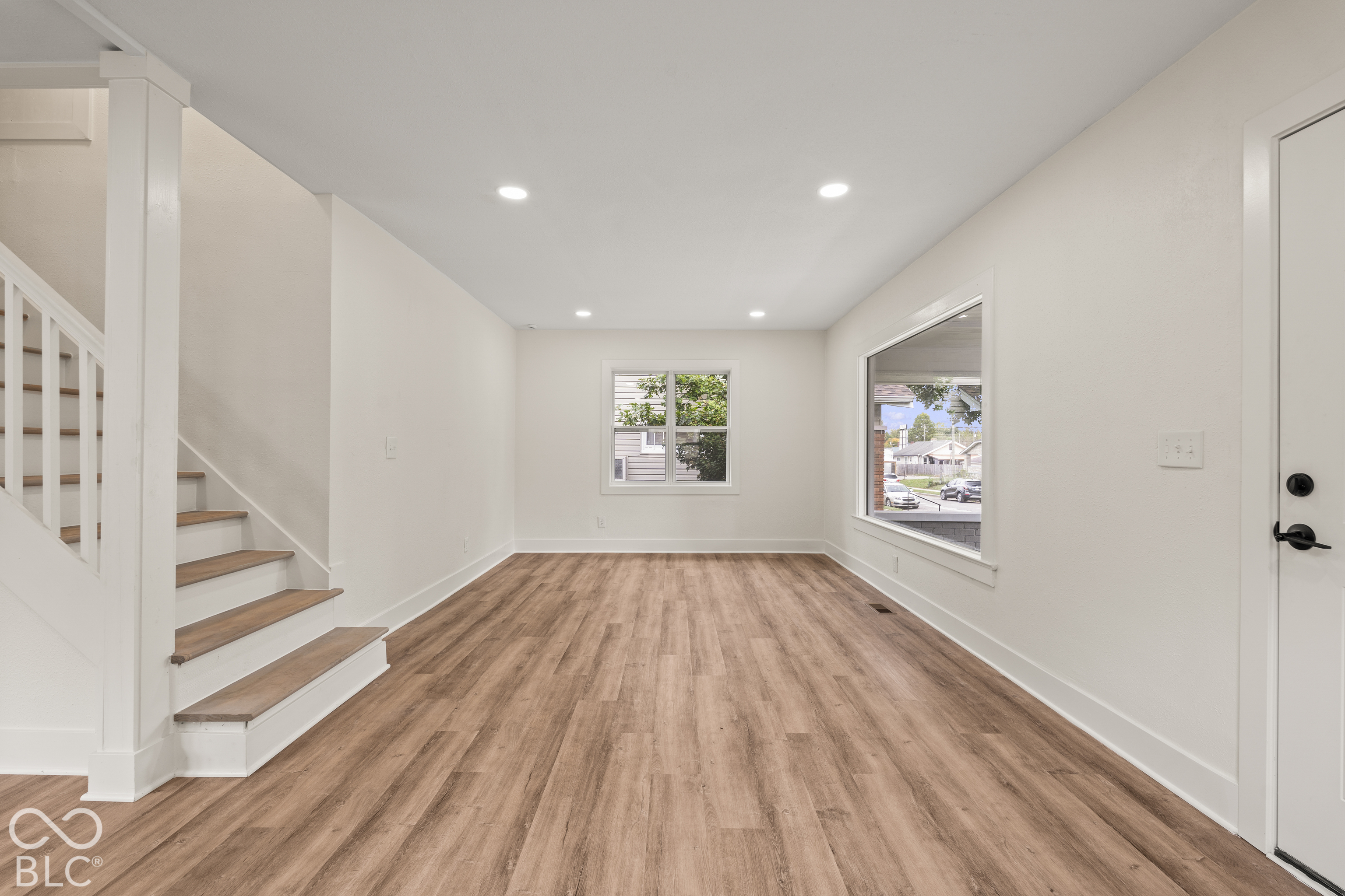 Neutral interior space featuring wood-finish flooring, recessed lighting, large picture windows, and a staircase with a white railing