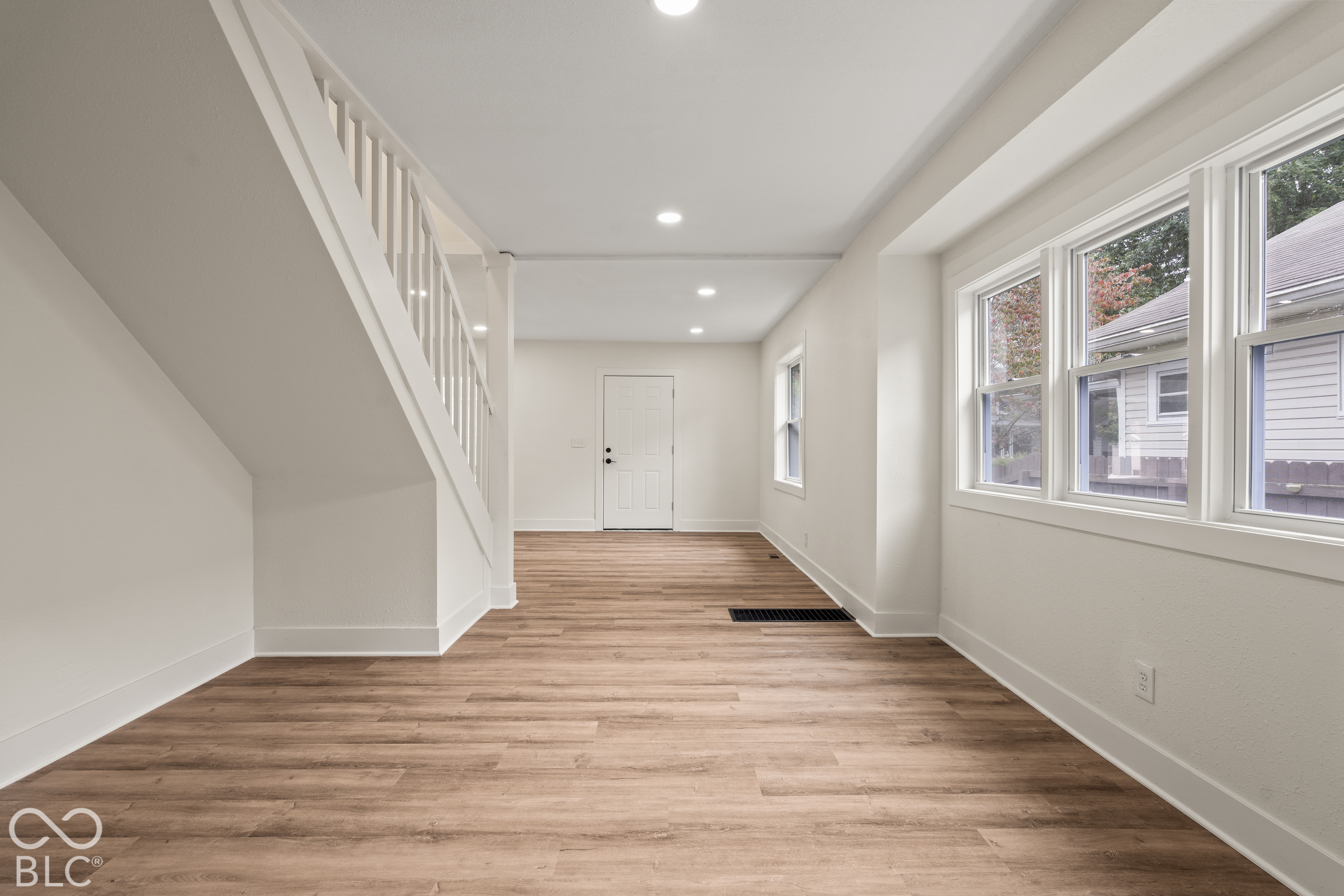 Neutral interior featuring wood-finish flooring, recessed lighting, white staircase railing, and large multi-pane windows