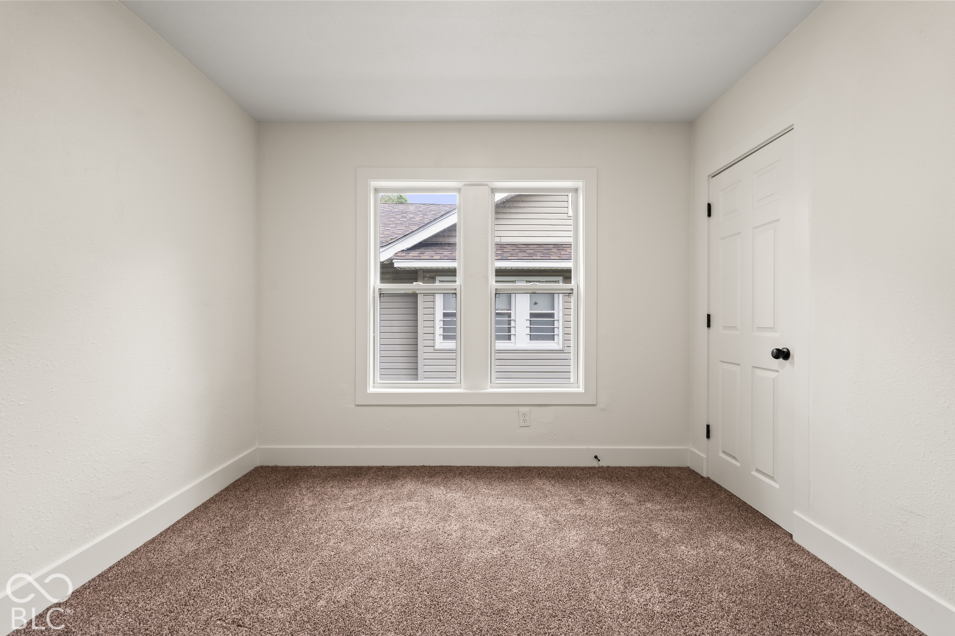 Neutral-toned room featuring neutral carpeting, a central double-pane window, and a white six-panel interior door with dark hardware