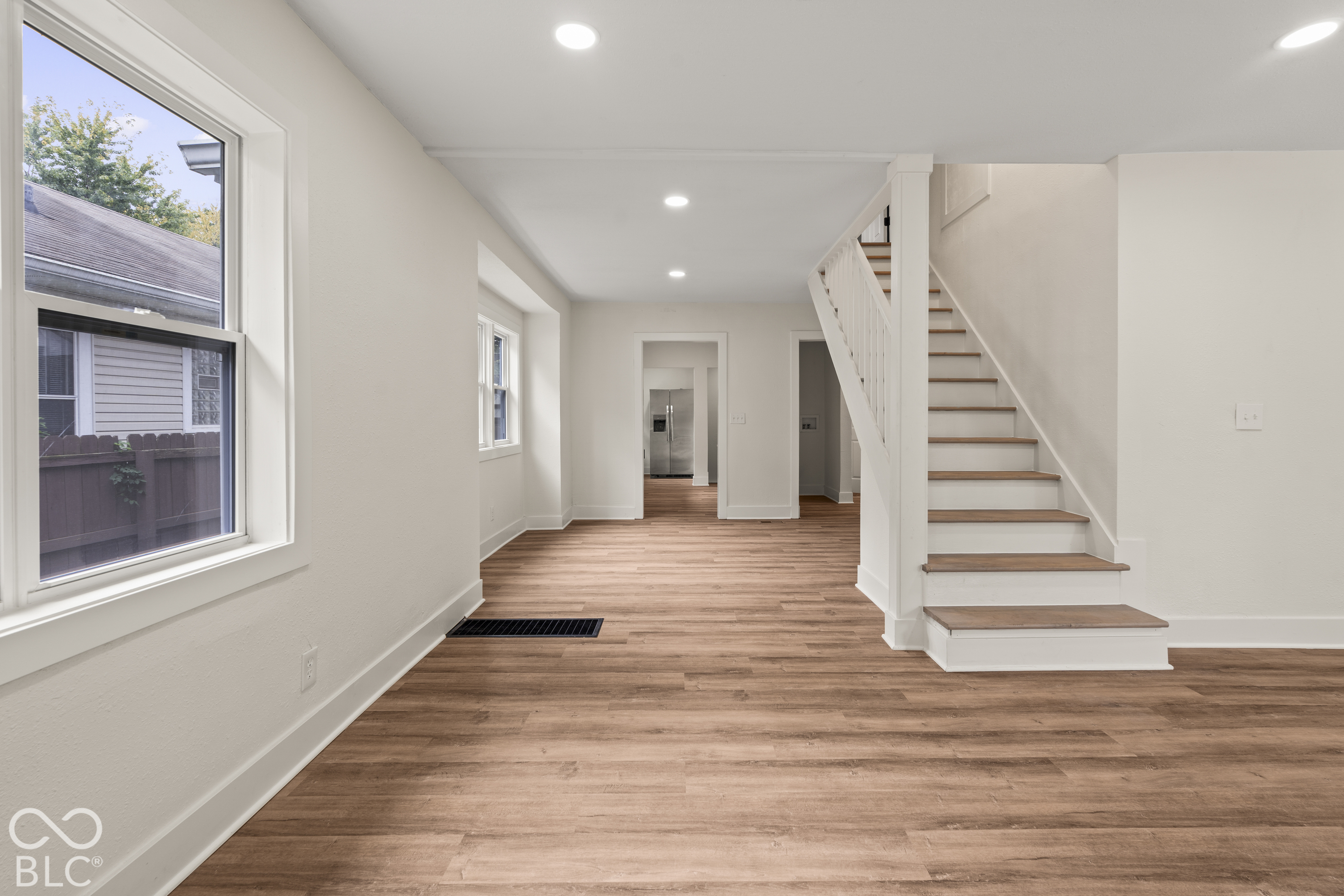 Interior space featuring wood-finish flooring, recessed lighting, white stairwell with wooden treads, and multi-pane windows